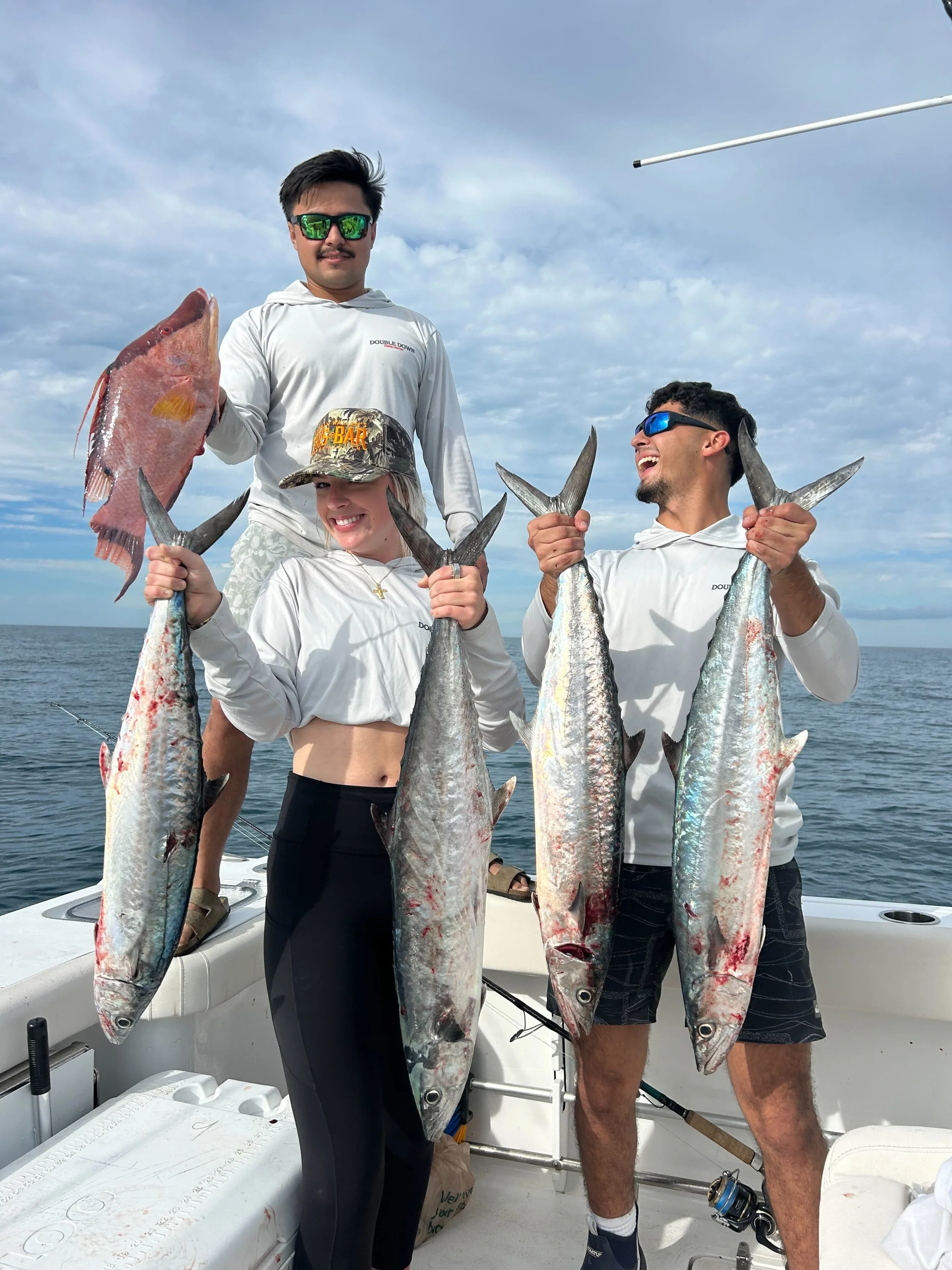 Close-up of a boat's cooler with a Double Down Fishing Charters logo, featuring palm trees and fish, with water and distant land visible in the background.