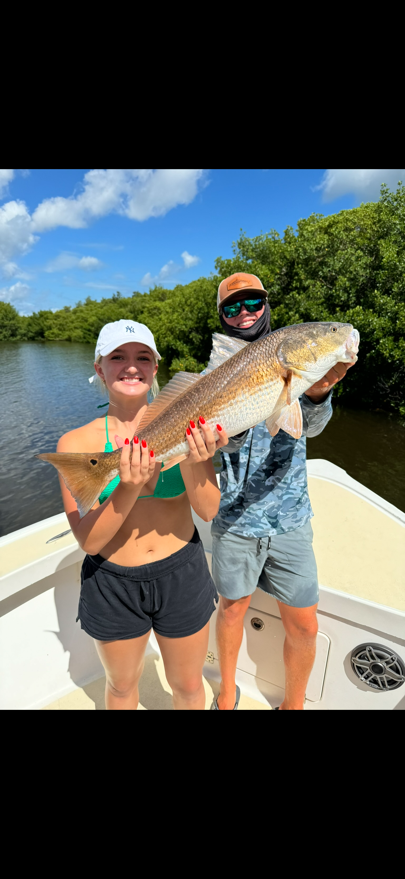 A man on a white fishing boat with a Yamaha outboard motor, operating the boat's controls in a body of water with a shoreline in the background.