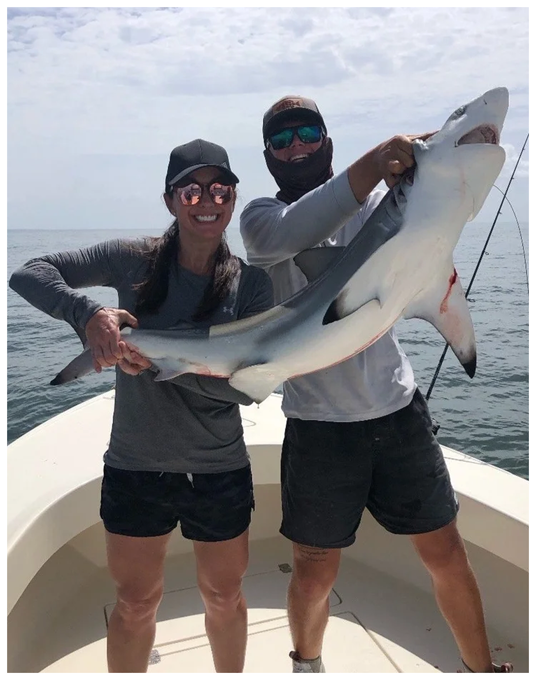 Two people on a fishing charter holding a shark over the water.