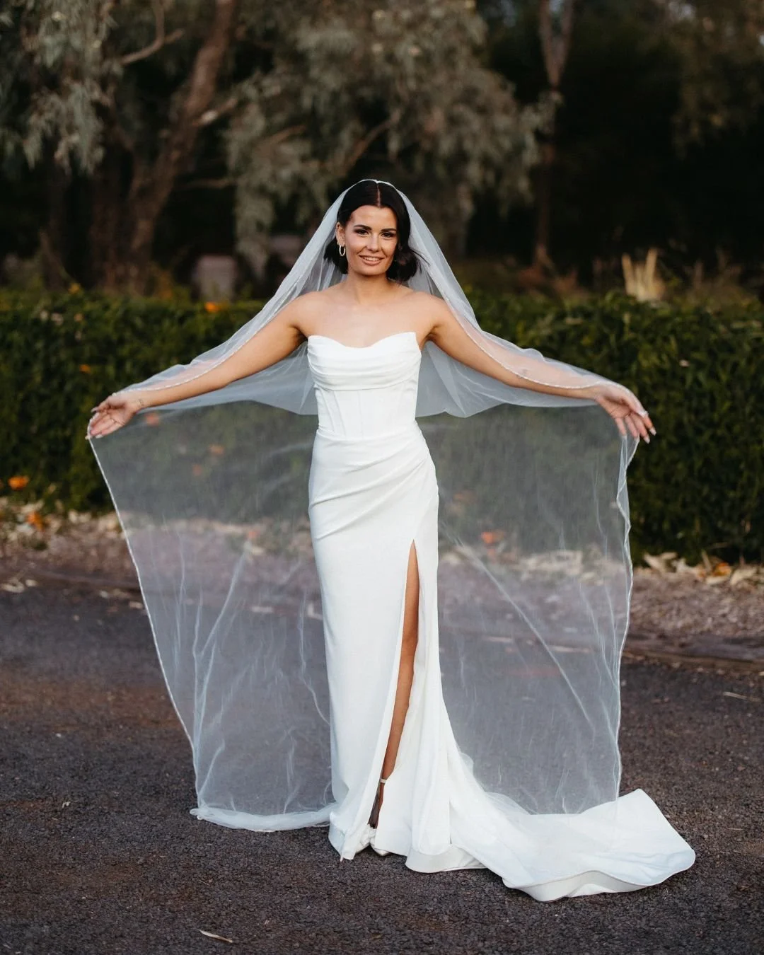 Real bride in a professionally altered wedding gown with a sleek fitted design,thigh-high slit, and long veil, highlighting expert bridal tailoring services.