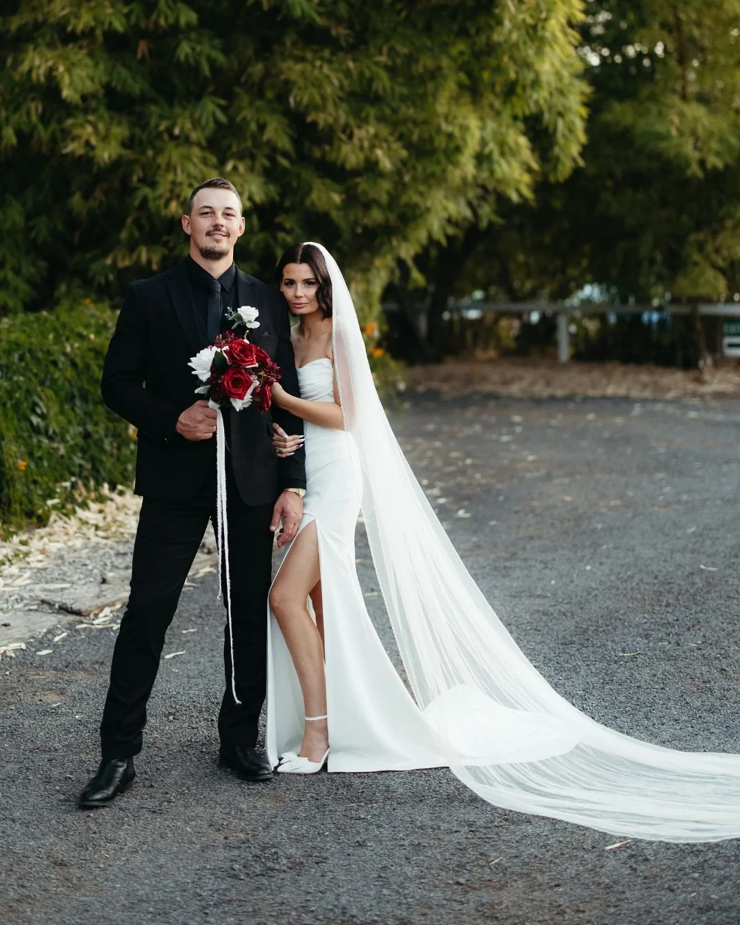 Real bride in a professionally altered wedding gown with a sleek fitted design,thigh-high slit, and long veil, highlighting expert bridal tailoring services.