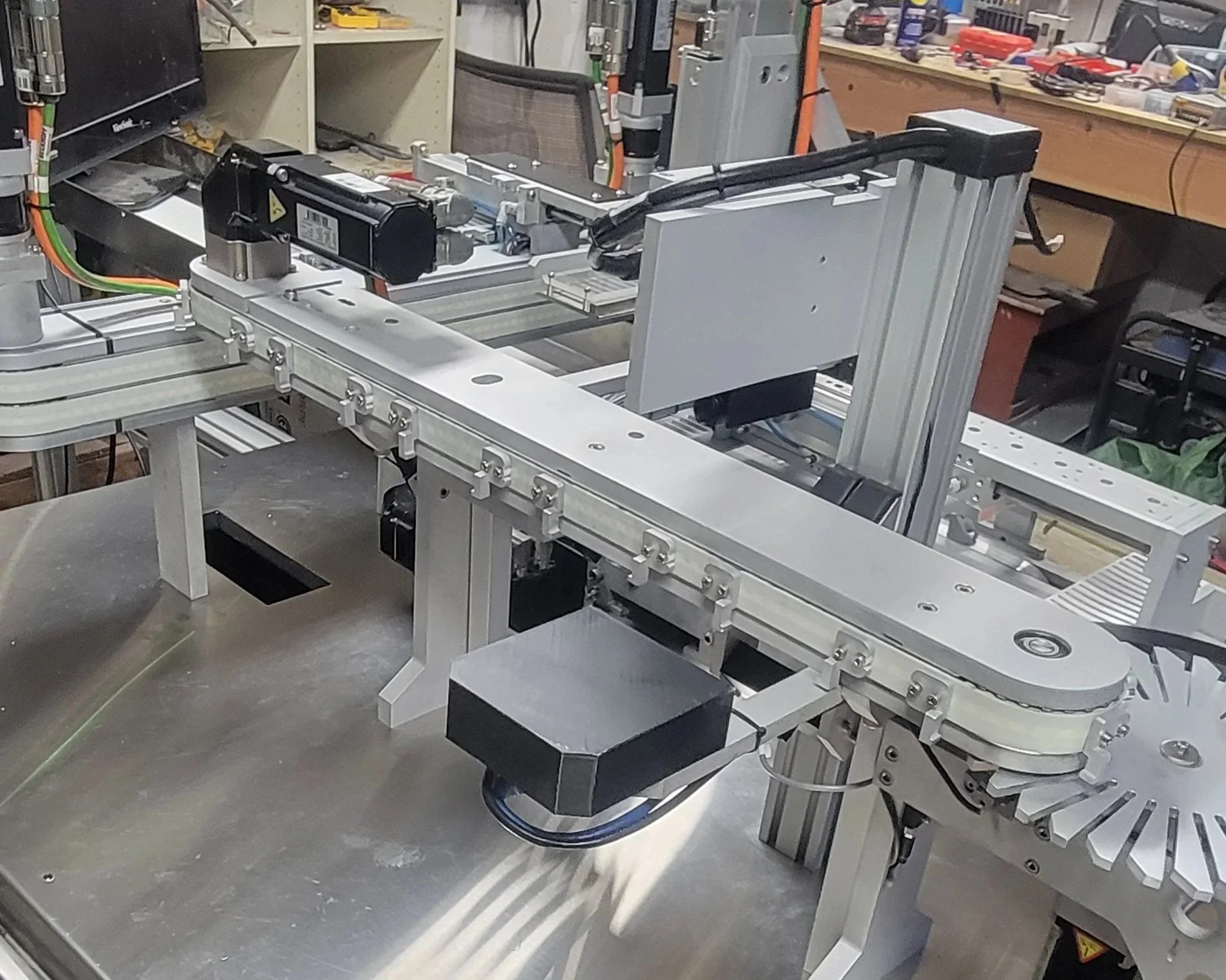 A robotic assembly machine with a sliding aluminum track and black motors in a workshop or lab environment.