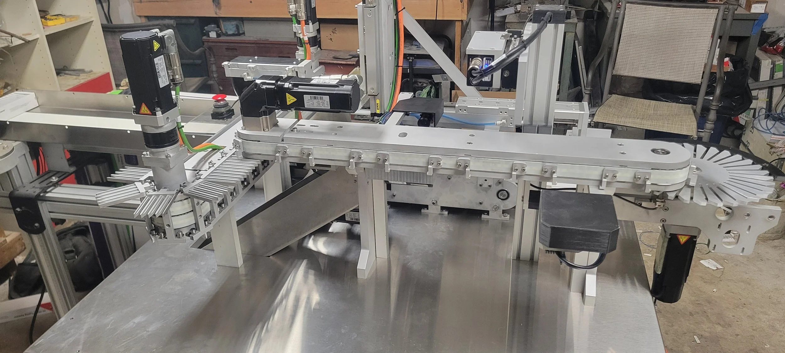 A close-up of an industrial machinery system with multiple black and silver components, including motors, rails, and a conveyor belt, set in a workshop or manufacturing environment. Beckhoff PLC, Allen Bradley, Siemens.