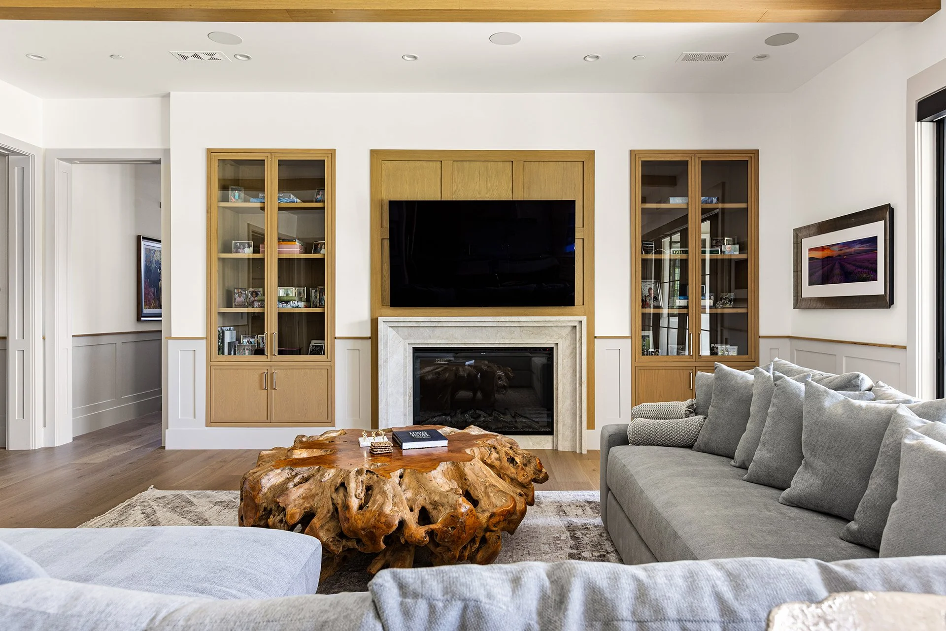 Living room with a gray sofa, a unique wooden coffee table, a fireplace, a large TV, and built-in cabinets.