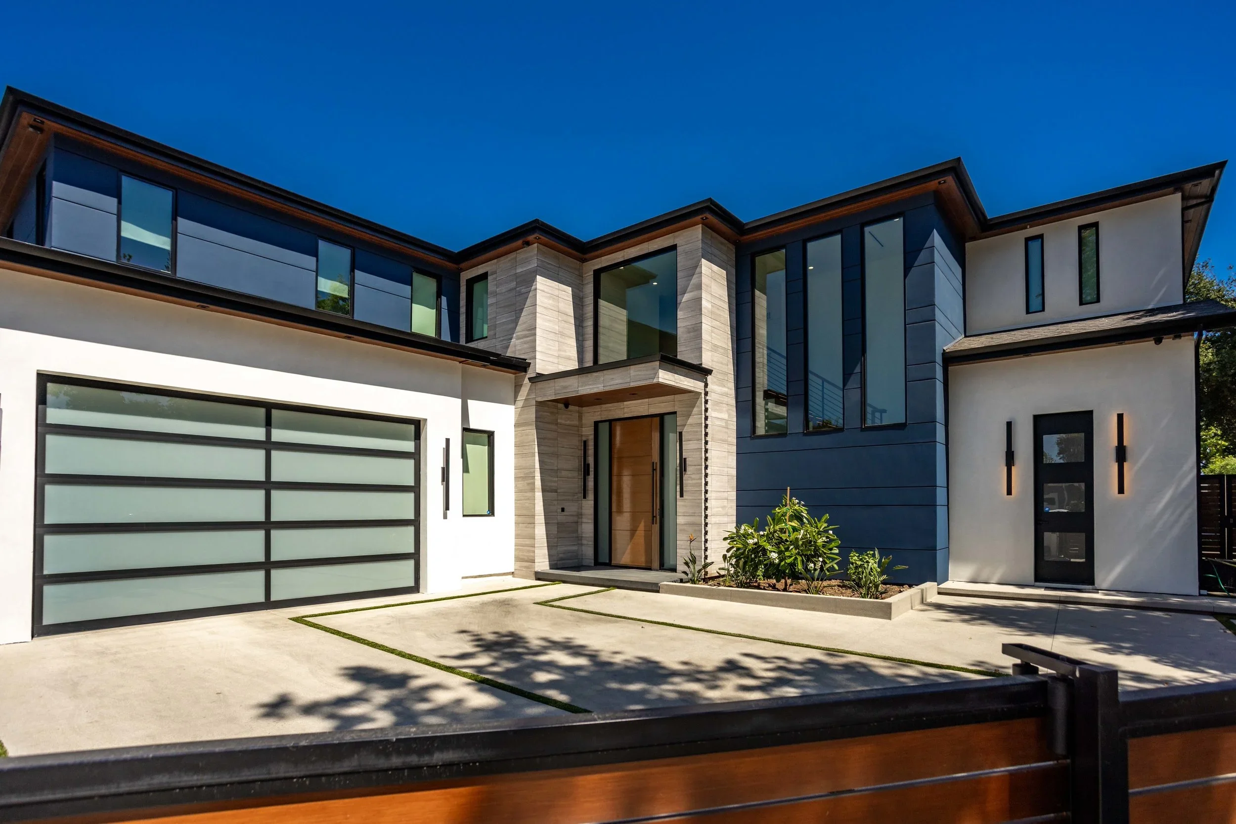 Modern living room with a large sectional sofa, entertainment center with TV, fireplace, decorative shelving, and floor-to-ceiling window opening to a backyard with a basketball hoop.
