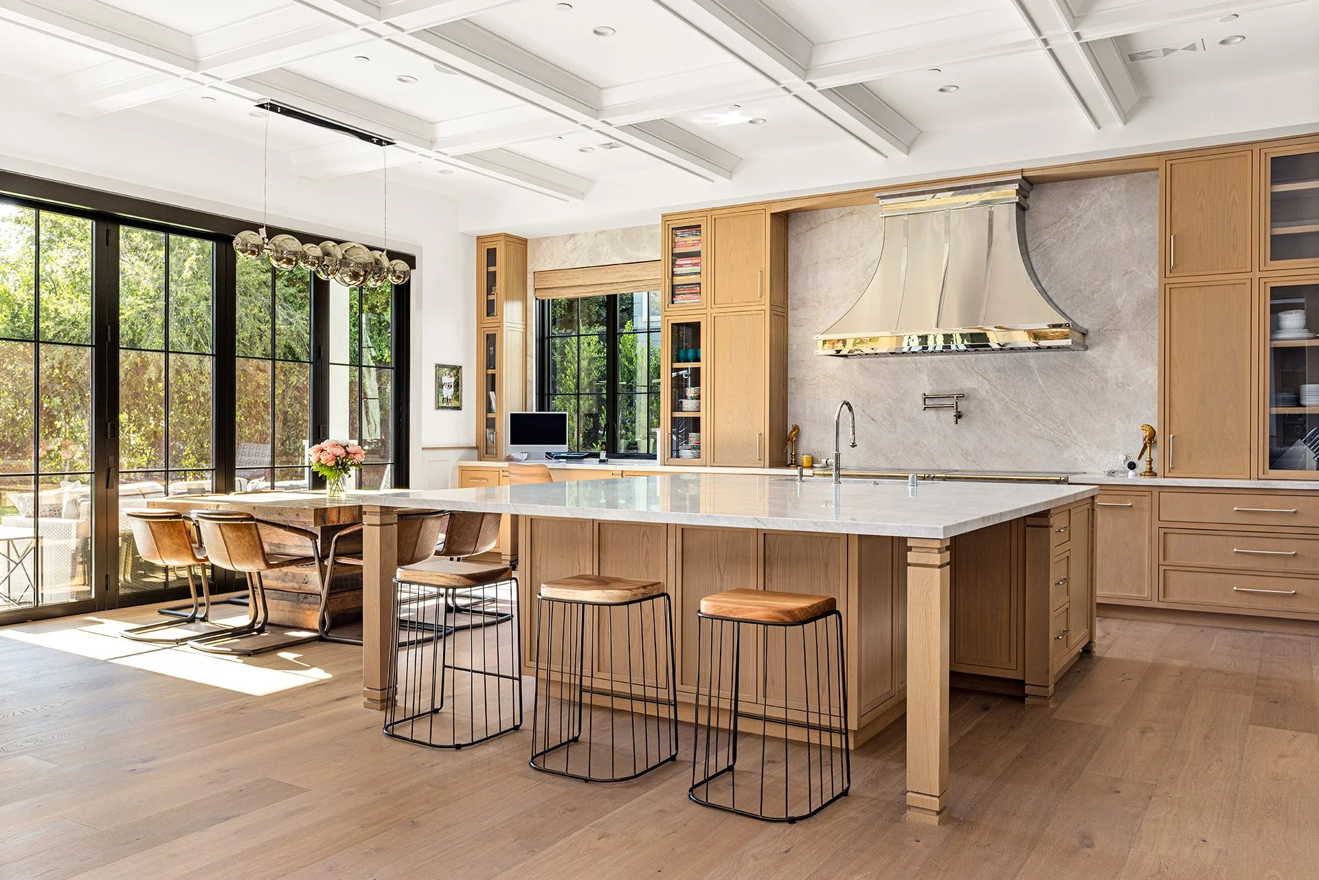Modern kitchen with large island, wooden cabinets, marble backsplash, and large windows with view of greenery.