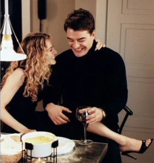 A man and woman laughing and enjoying drinks at a dinner table in a cozy home setting.