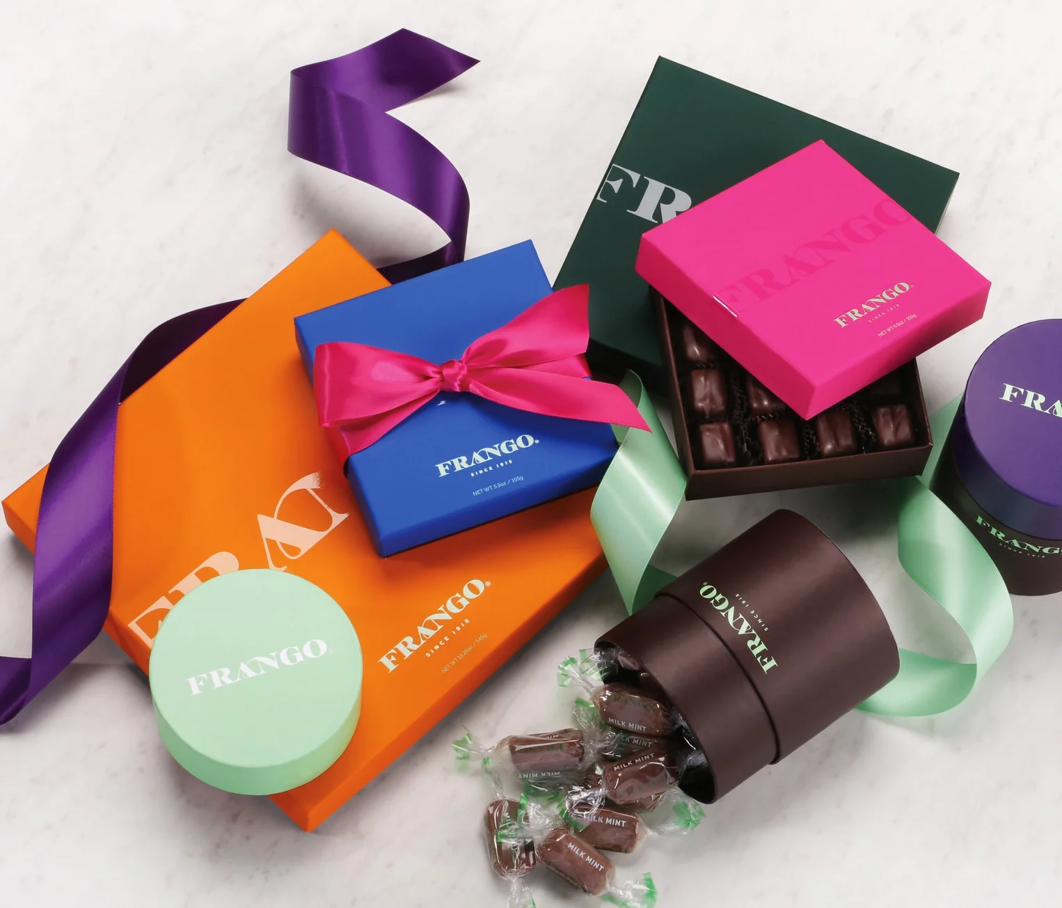 Assorted Frango chocolate gift boxes with ribbons and wrapped candies on a marble surface.