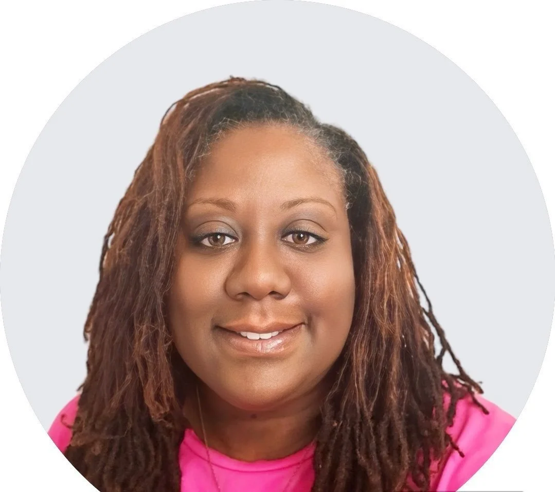 Professional headshot of a woman with long dreadlocks wearing a pink top, smiling against a light gray background.