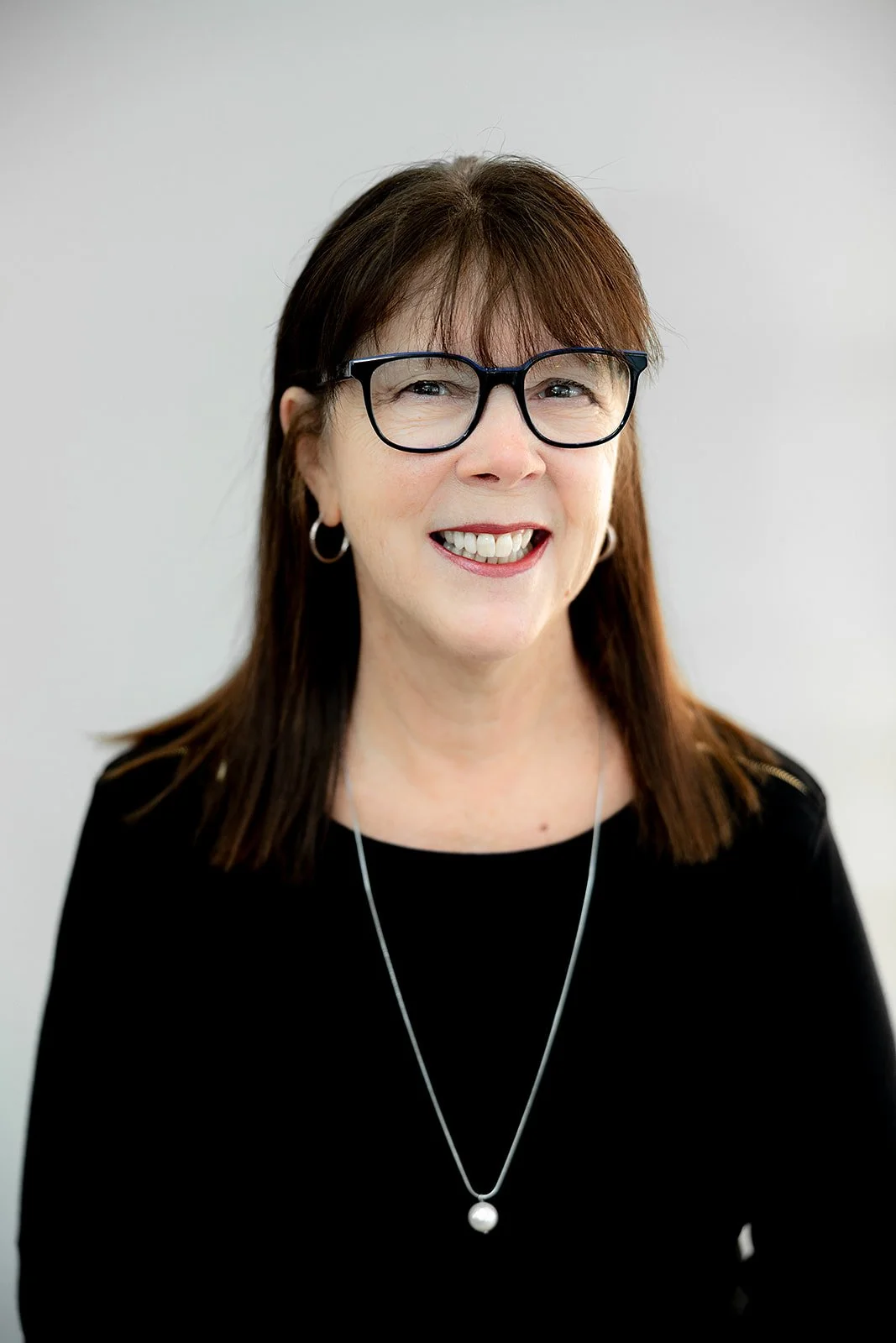 A woman with glasses smiling in front of display shelves full of glasses and sunglasses in an optical store.