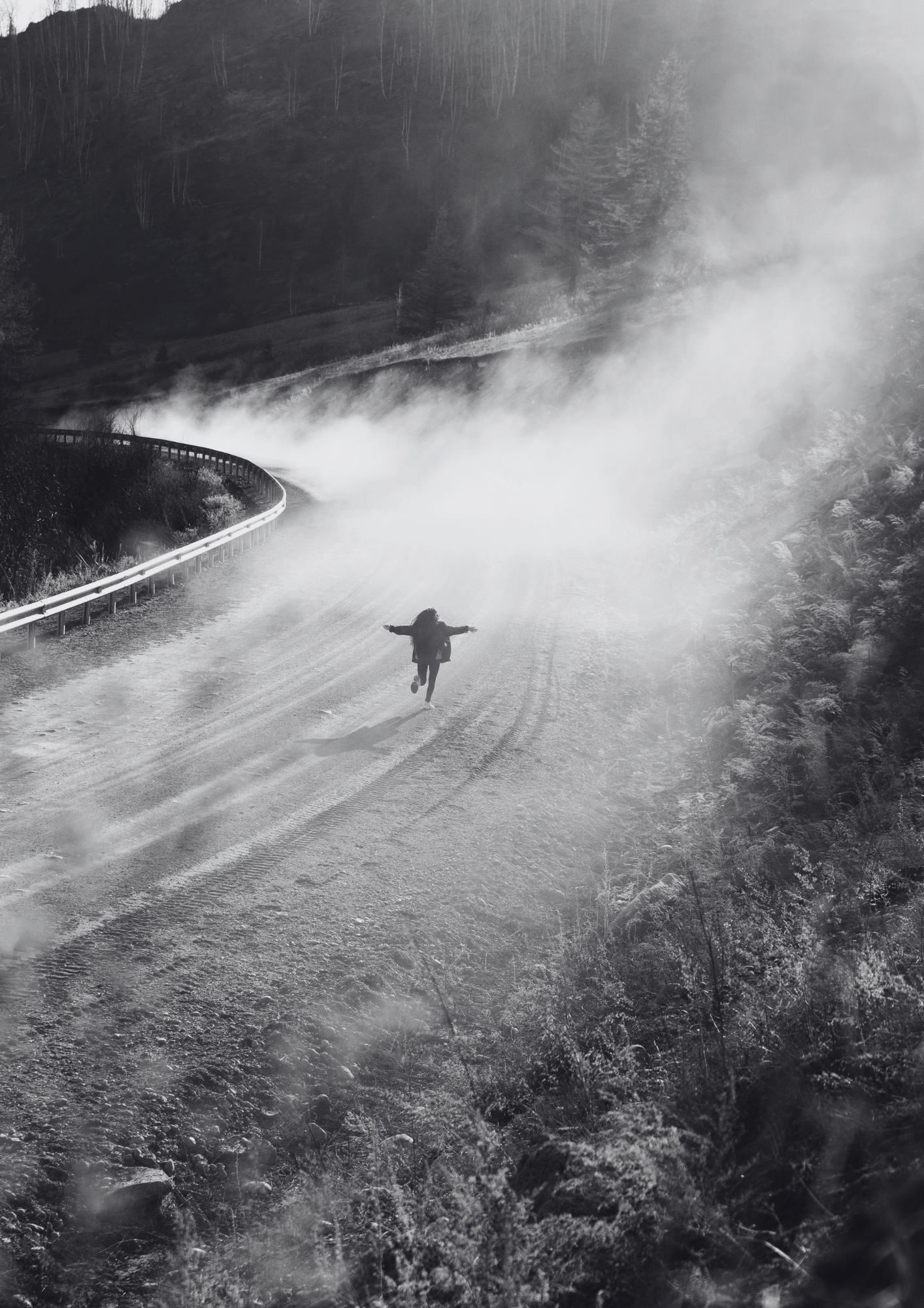 Person running on a misty dirt road, surrounded by trees and hills, in black and white.