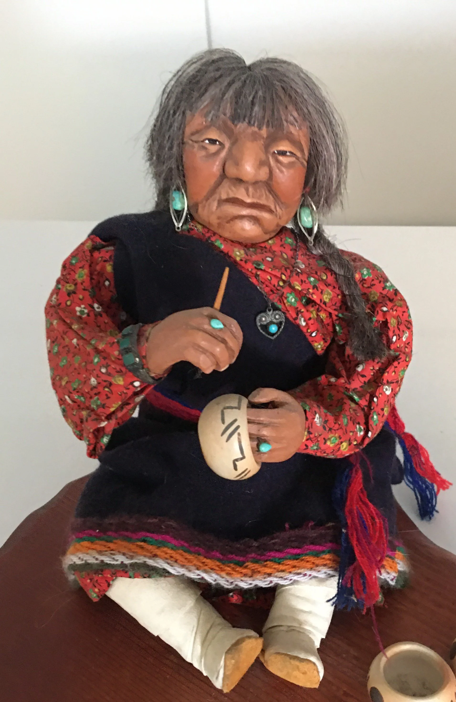 Hopi potter with high mocassins, black skirt, red top with woven black sash.  Wearing turquoise earrings. Painting pot. carved by Shona Hah  1970  3.JPG