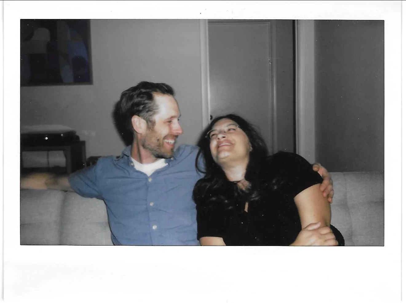 Couple sitting on couch at home and smiling at each other, shot on instax wide