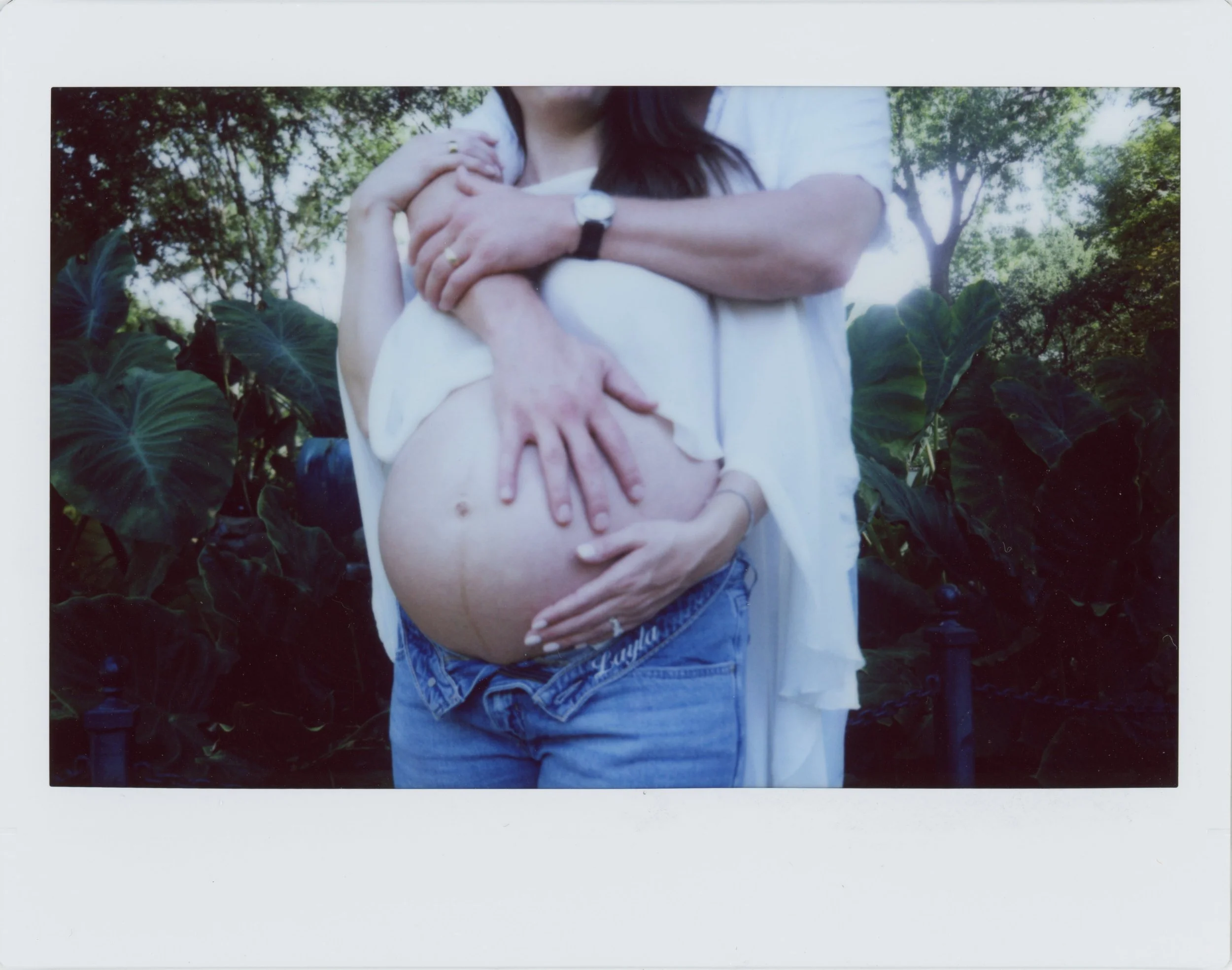 Couple holding belly and hugging during maternity session at Grapevine Botanical Gardens in Grapevine, Texas shot on instax wide