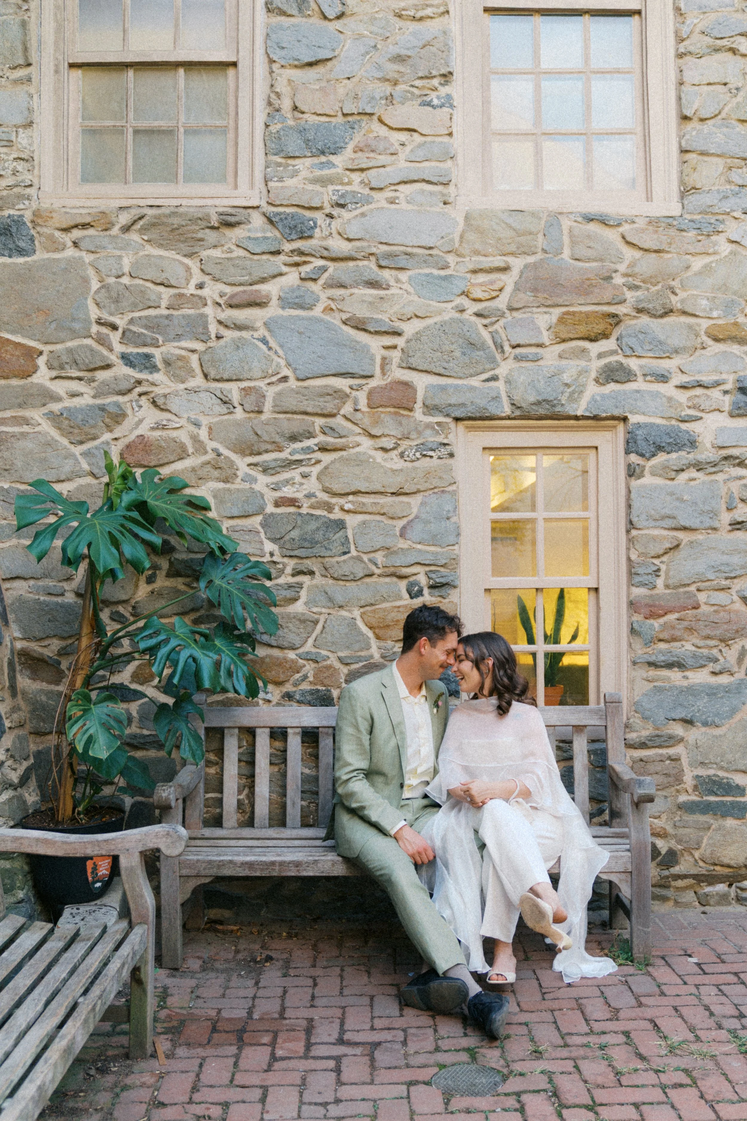 newly married couple sitting on bench at old stone house courtyard georgetown washington dc