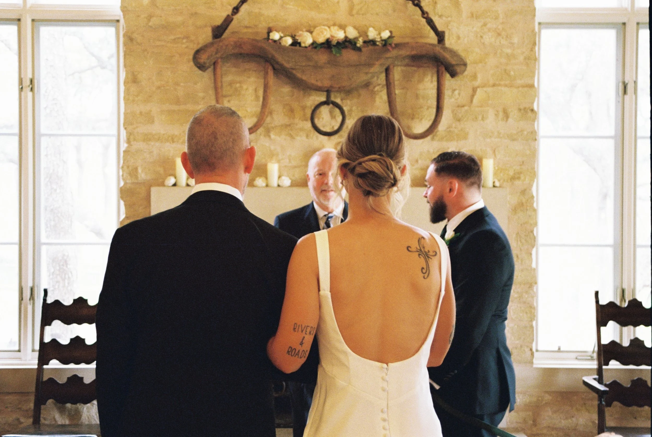 Father walking bride down the aisle arm in arm, angle from behind them, shot on 35mm film