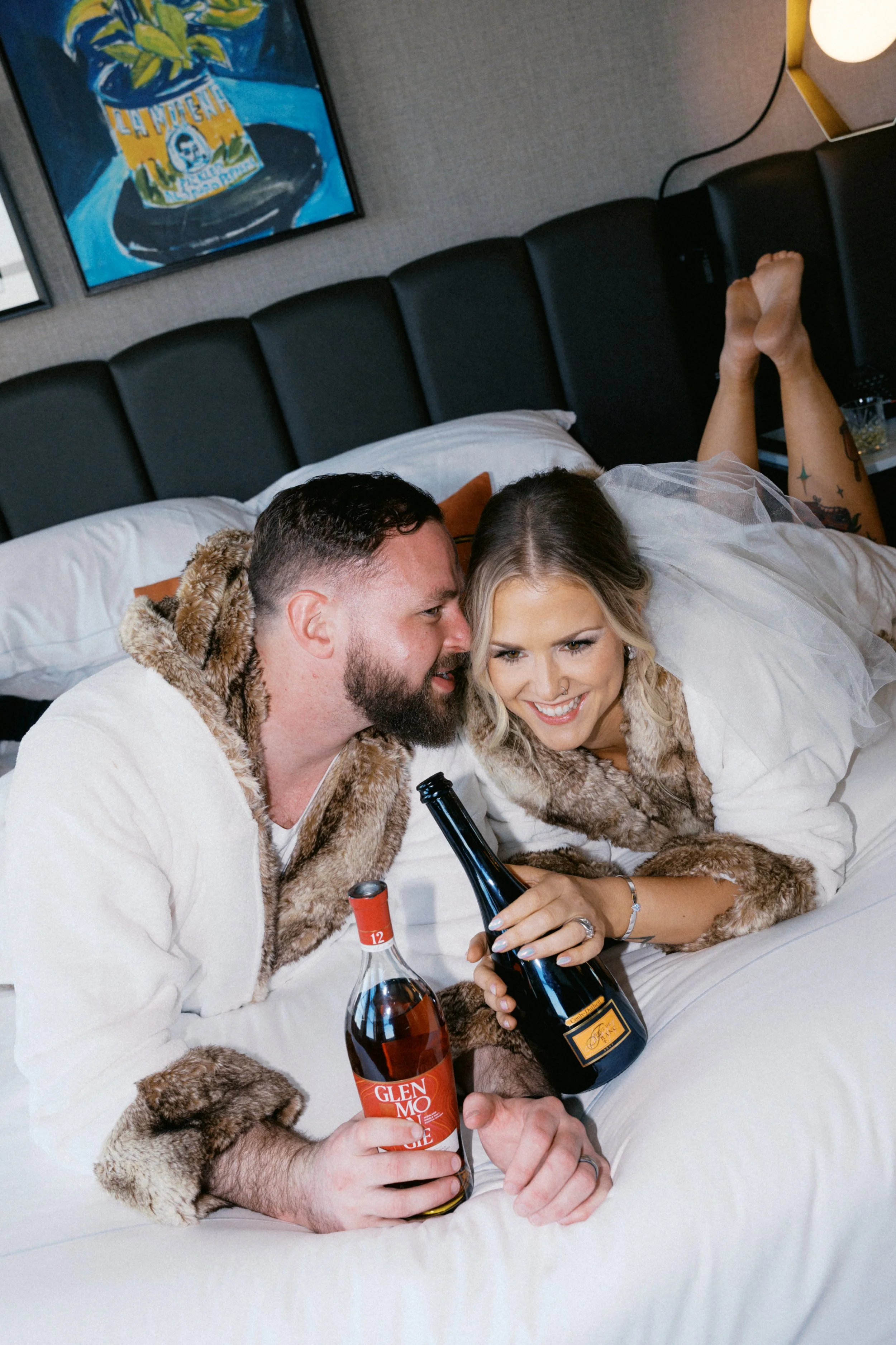 Couple drinking wine and wearing robes in bed at Kimpton Harper Hotel