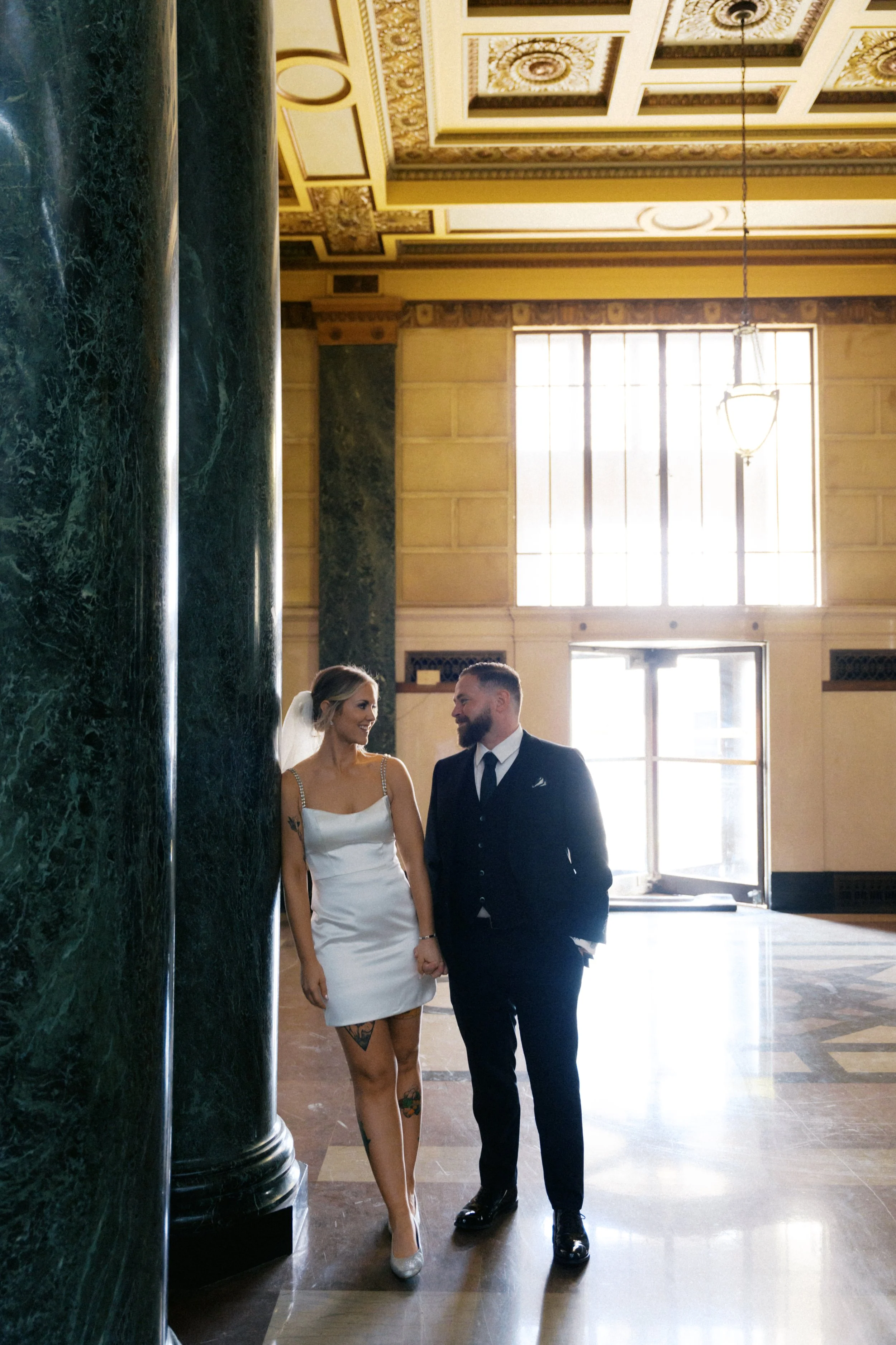 Bride and groom standing beneath historic architecture in Fort Worth