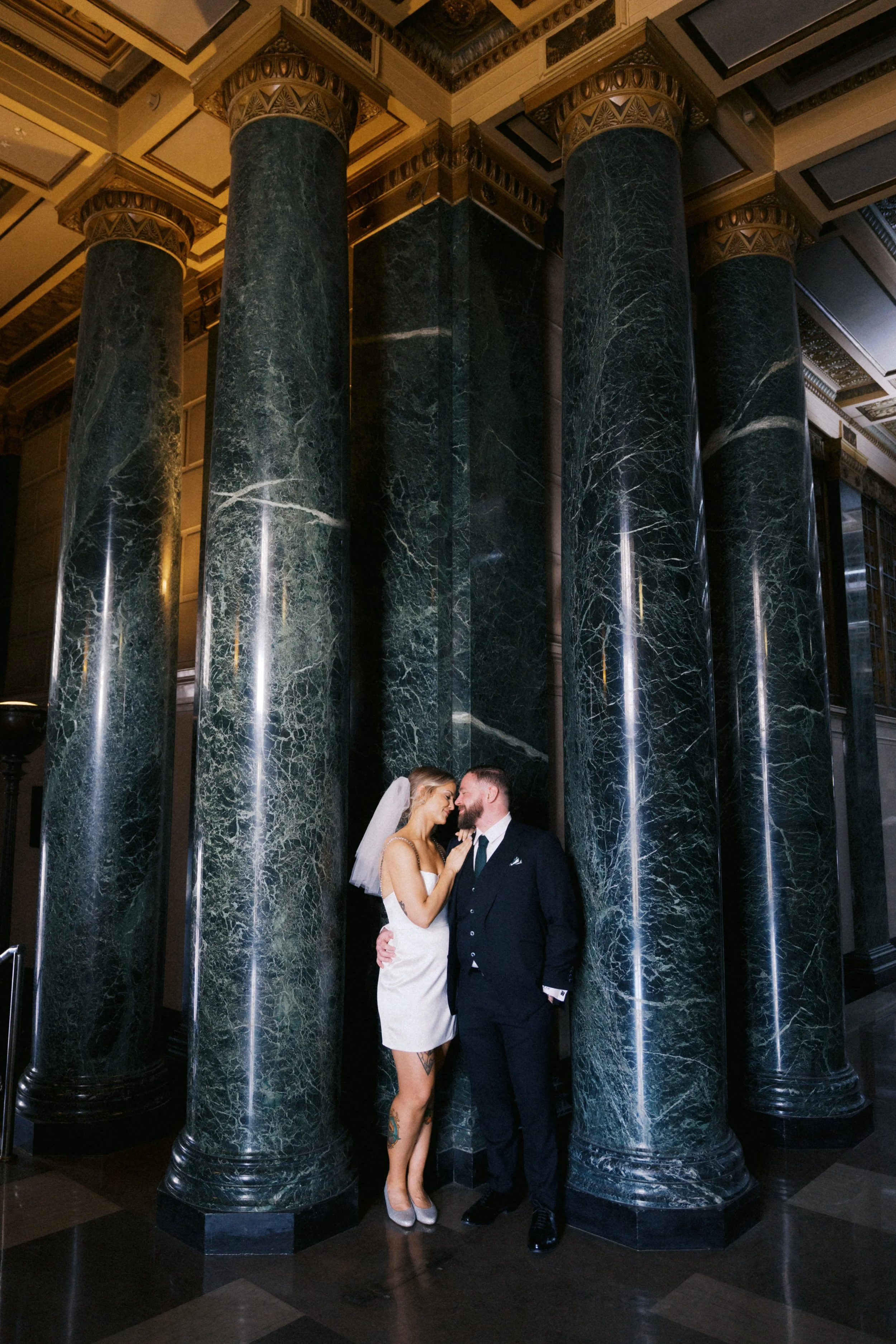 Bride and groom standing beneath historic architecture in Fort Worth
