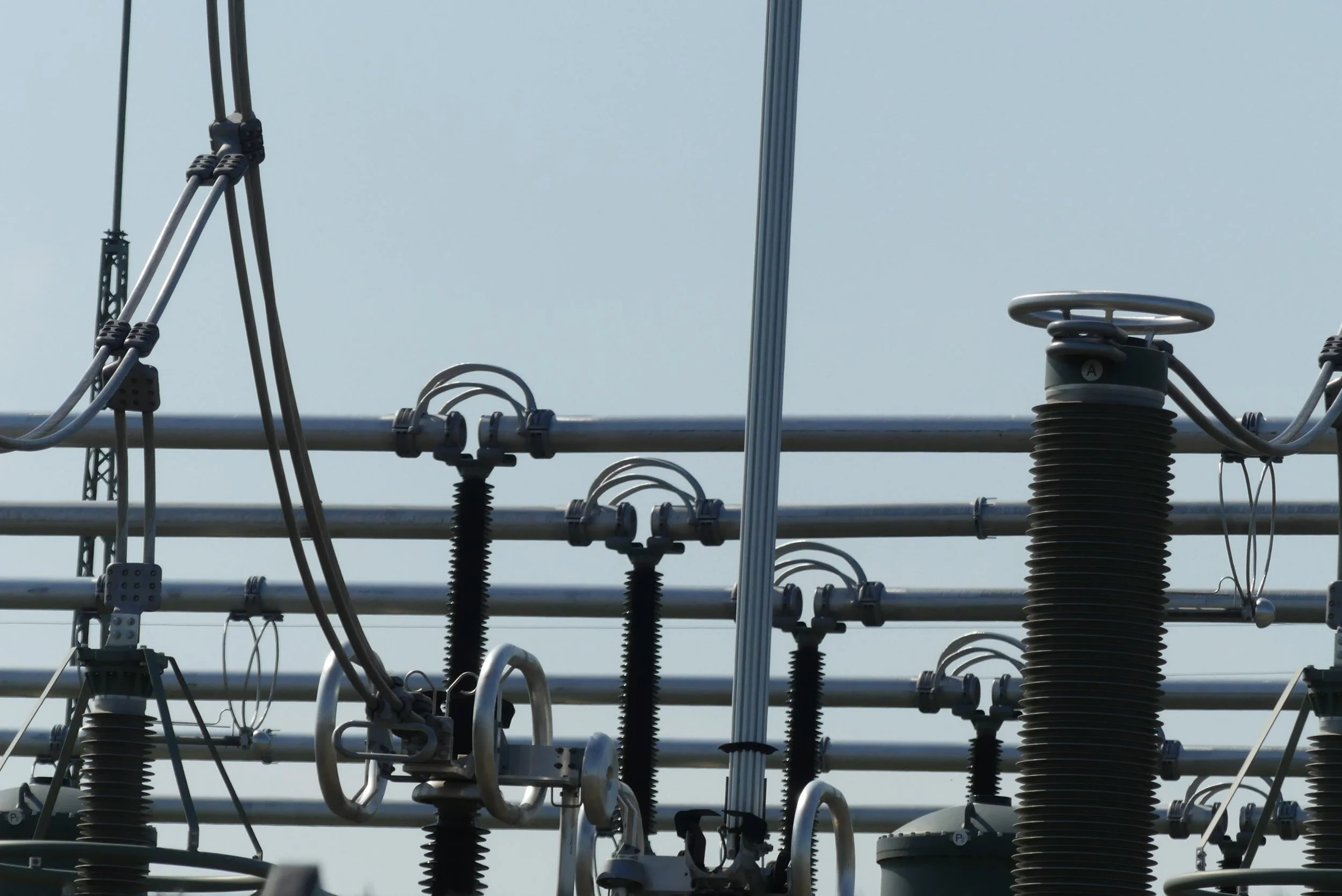 Close-up of electrical equipment and insulators on a power transmission tower with wires and sky in the background