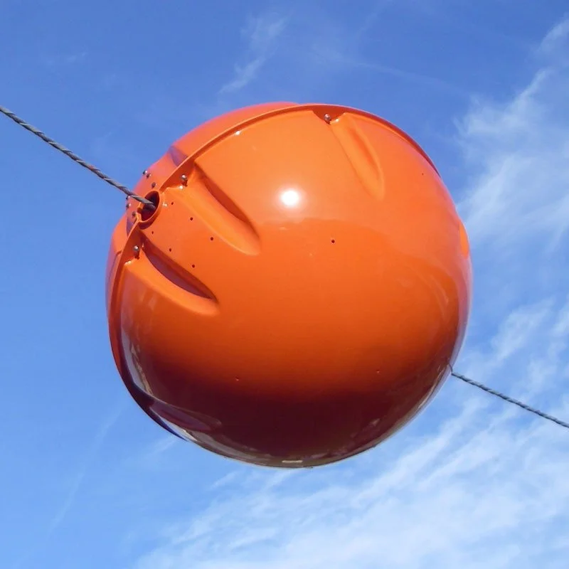 An orange spherical object, likely a buoy, tethered to a rope in the sky with some clouds and contrails visible.