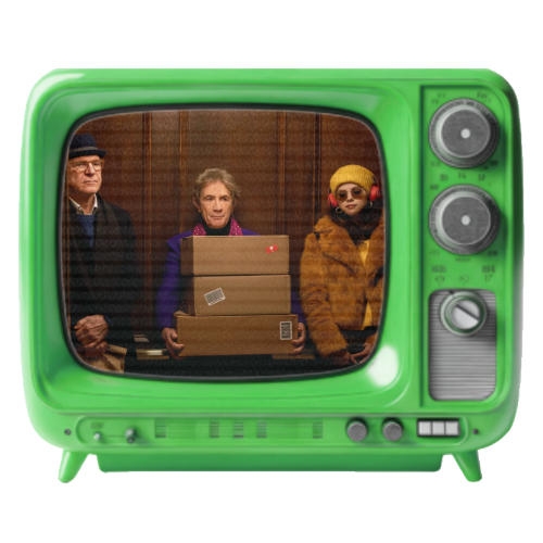 Three people standing behind a vintage green television set, with one holding cardboard boxes. The background appears to be a wooden wall.