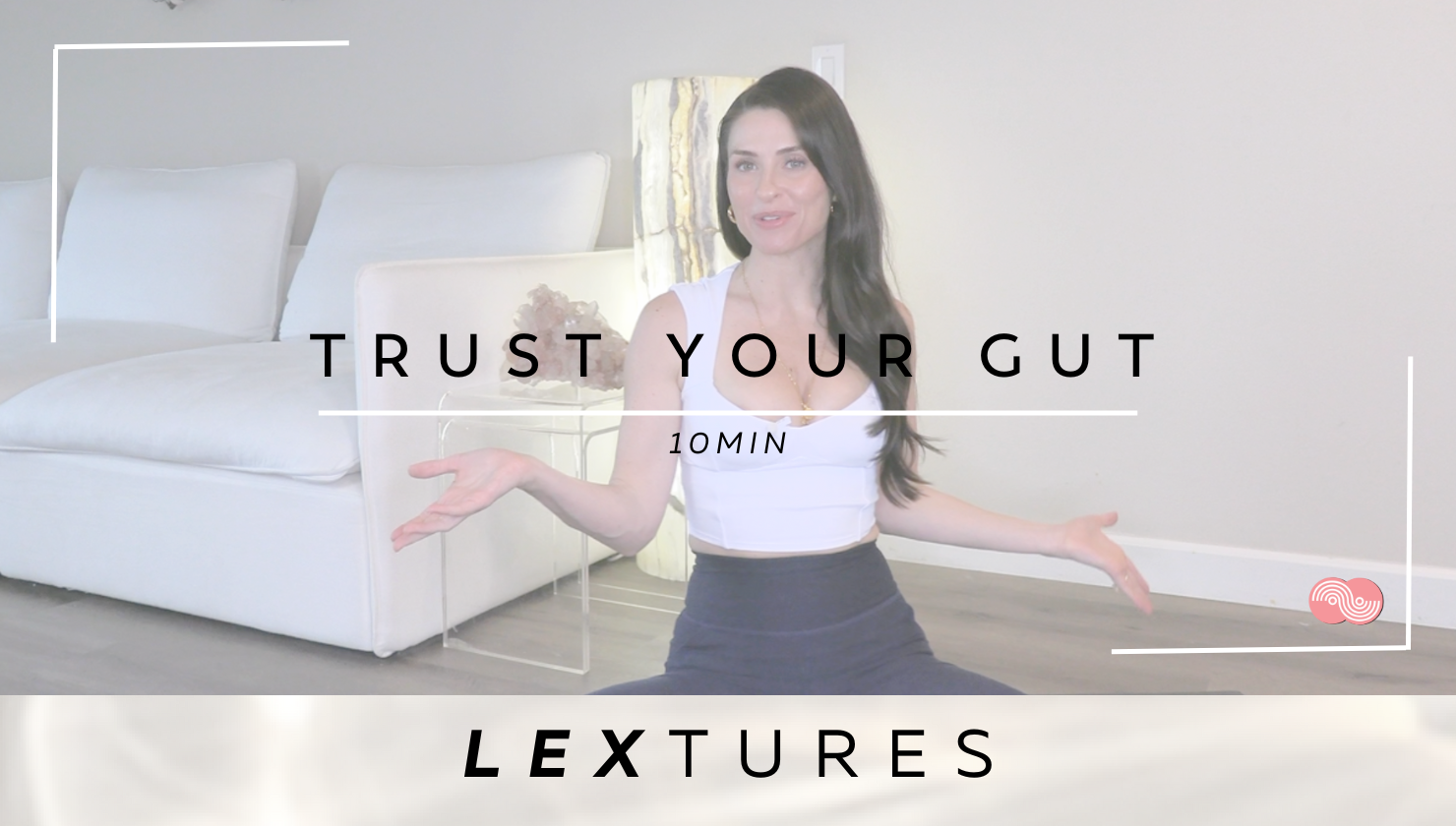 A woman sitting on the floor in a living room during a wellness video titled 'Trust Your Gut,' with the subtitle '10 Min' and the label 'LexTures' at the bottom. She has long dark hair and is wearing a white top and black pants.