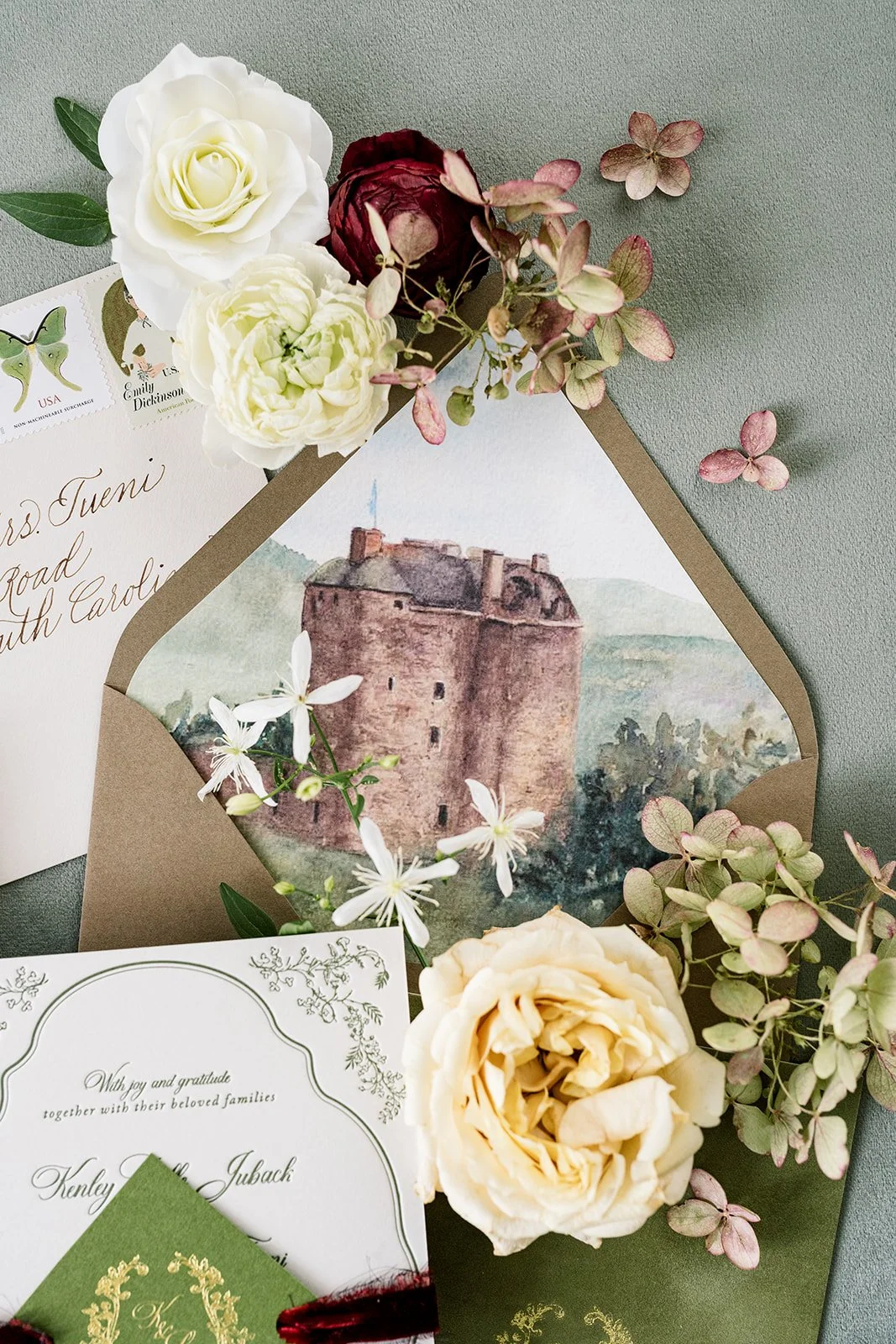 Flat lay with flowers, wedding invitation, and a watercolor envelope with Neidpath Castle in Scotland watercolor painting.