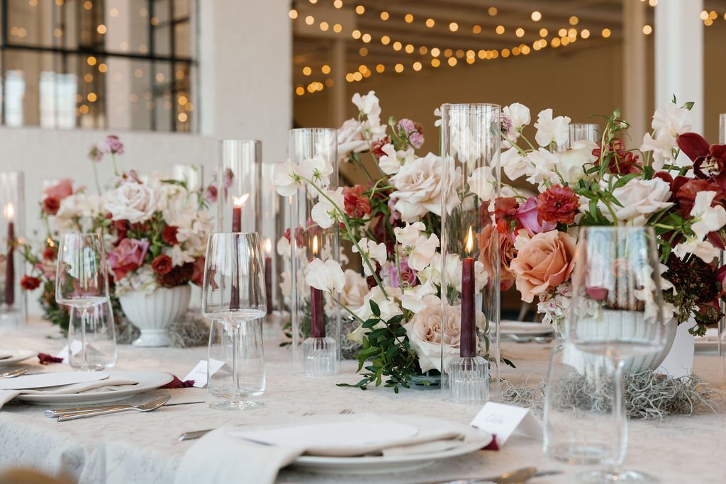 A wedding reception dining table with floral centerpieces, candles, wine glasses, and place settings, set for an elegant wedding.