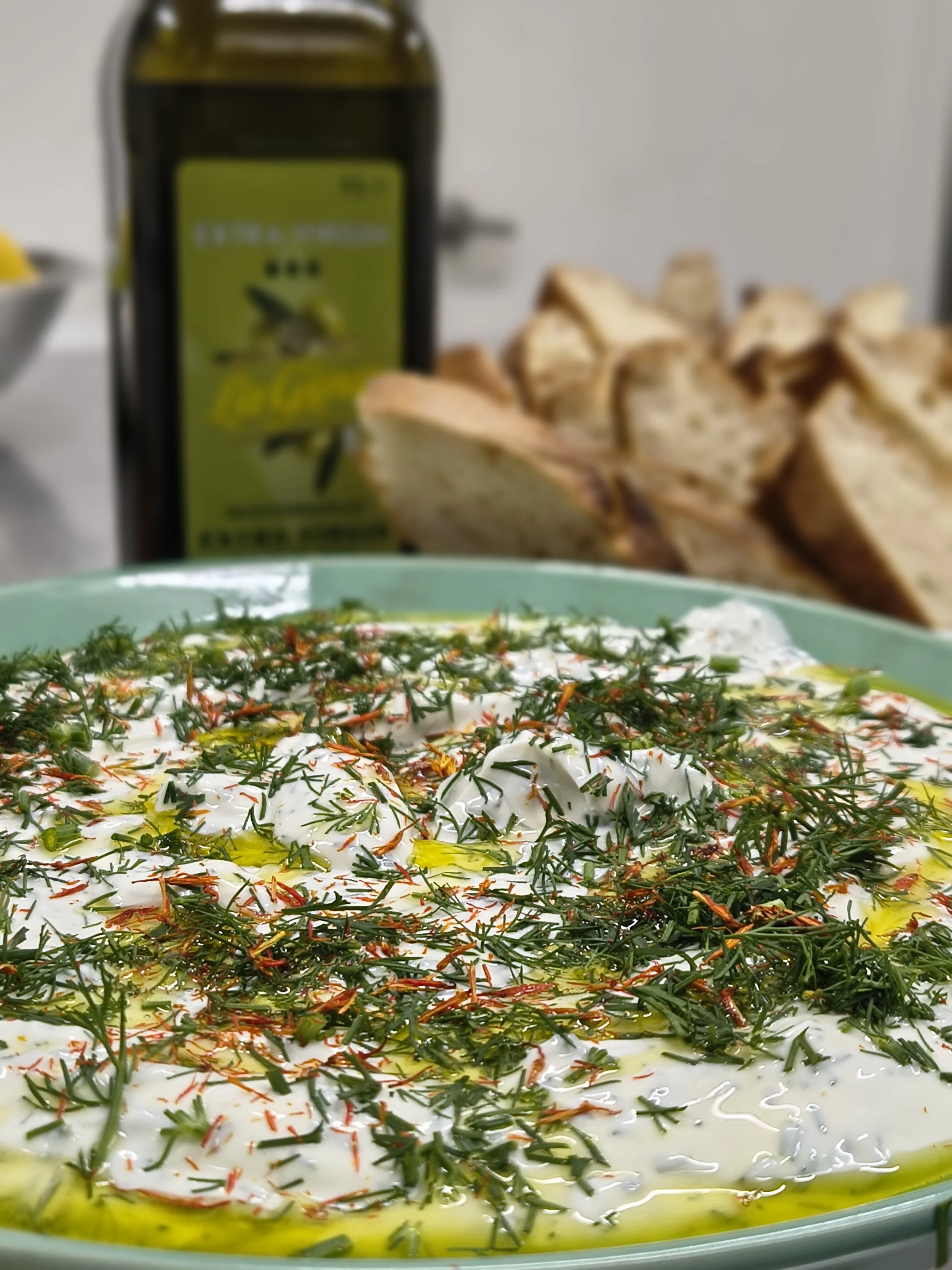 A dish of Persian herb and yogurt dip topped with chopped herbs and saffron threads, served in a glass bowl with olive oil drizzled on top.