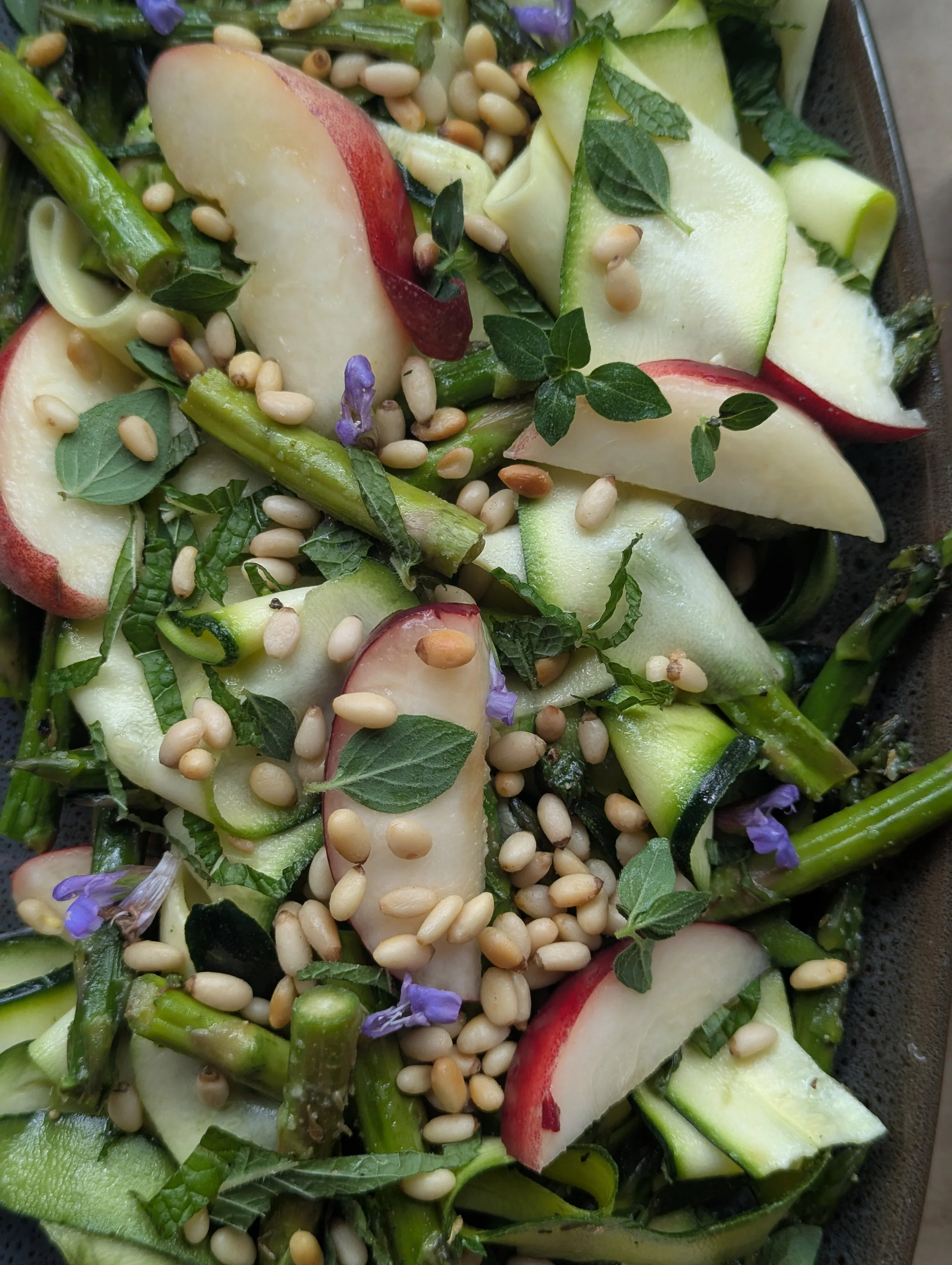 Salad with sliced apples, green beans, pine nuts, fresh herbs, and purple edible flowers.