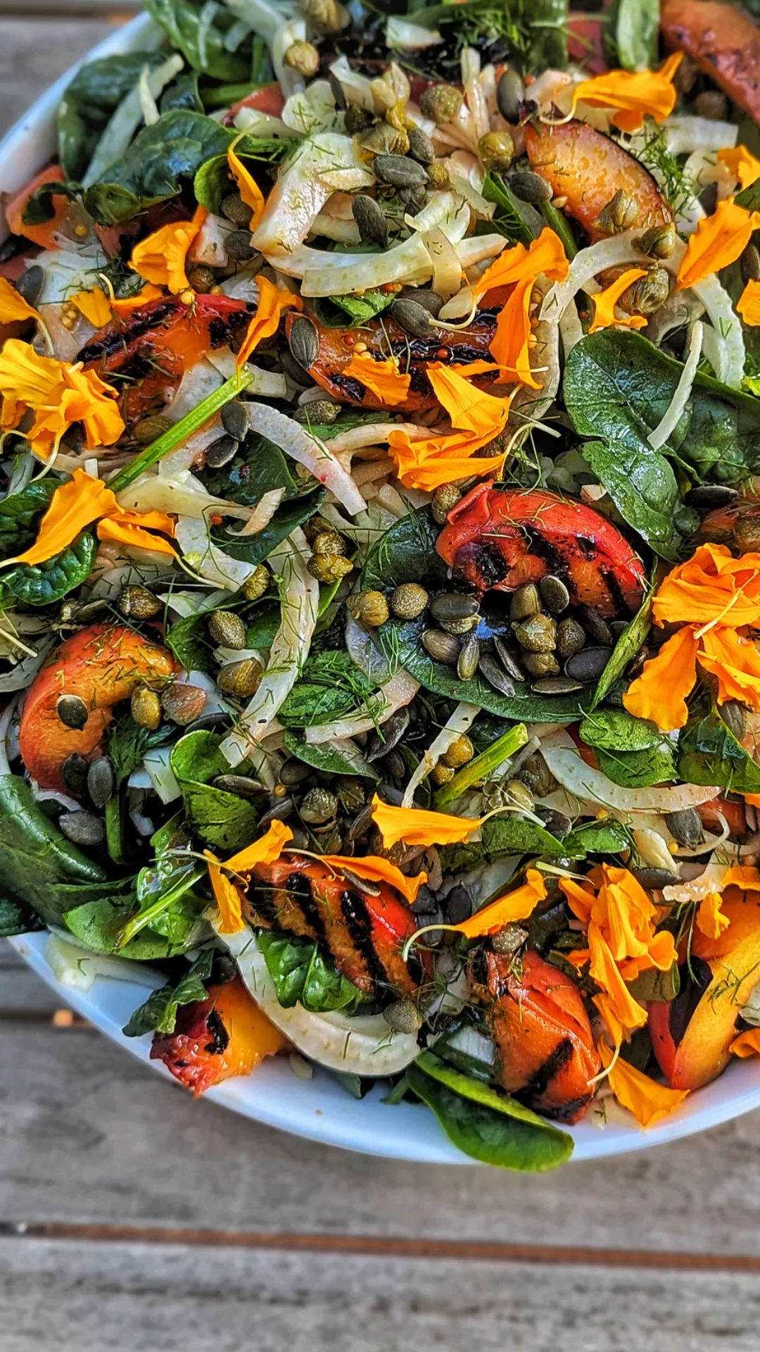A bowl of mixed salad with leafy greens, cherry tomatoes, pumpkin seeds, edible flowers, and thinly sliced vegetables.