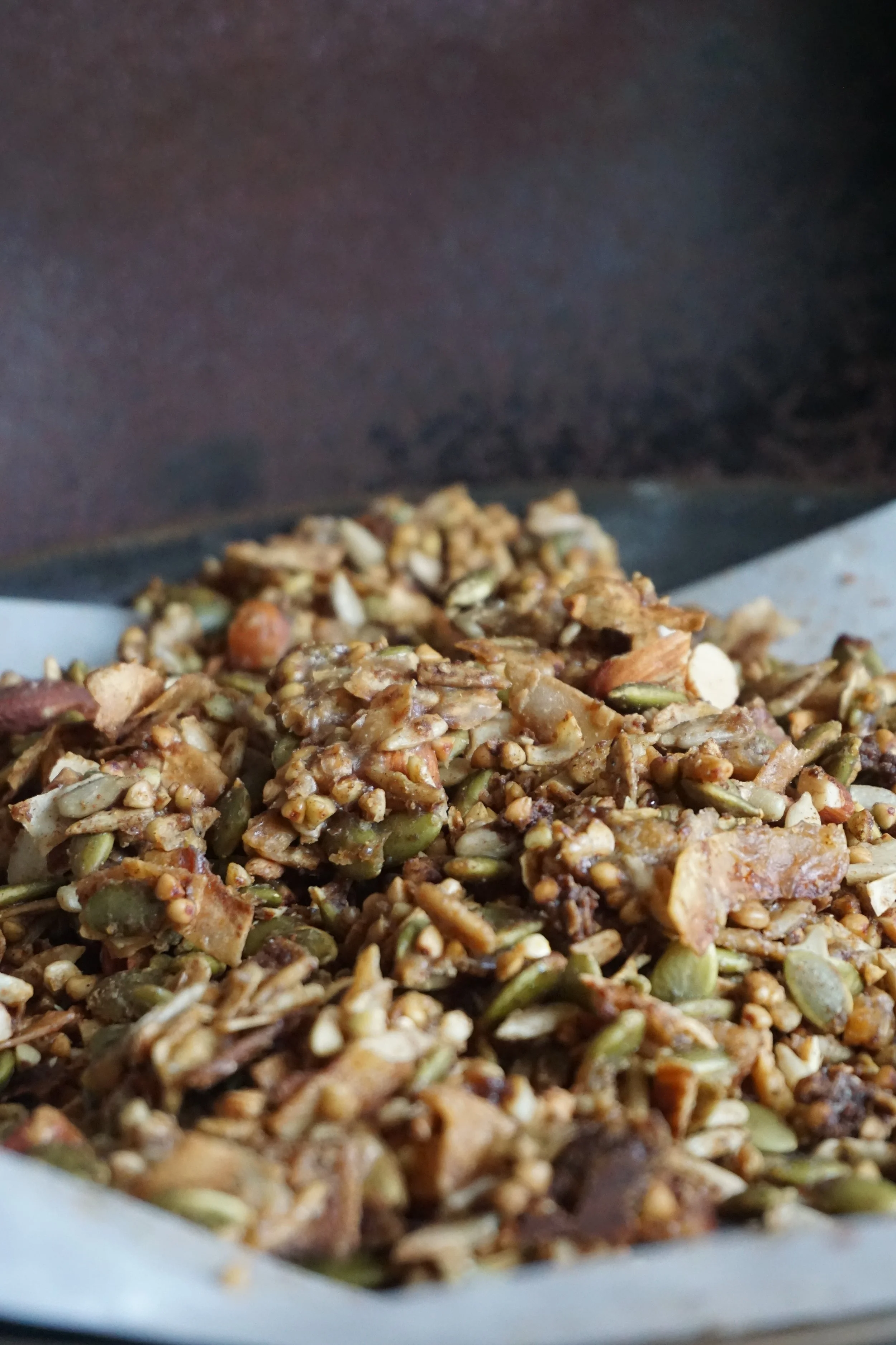 Close-up of granola with seeds, nuts, and dried fruit on a parchment paper-lined baking sheet.