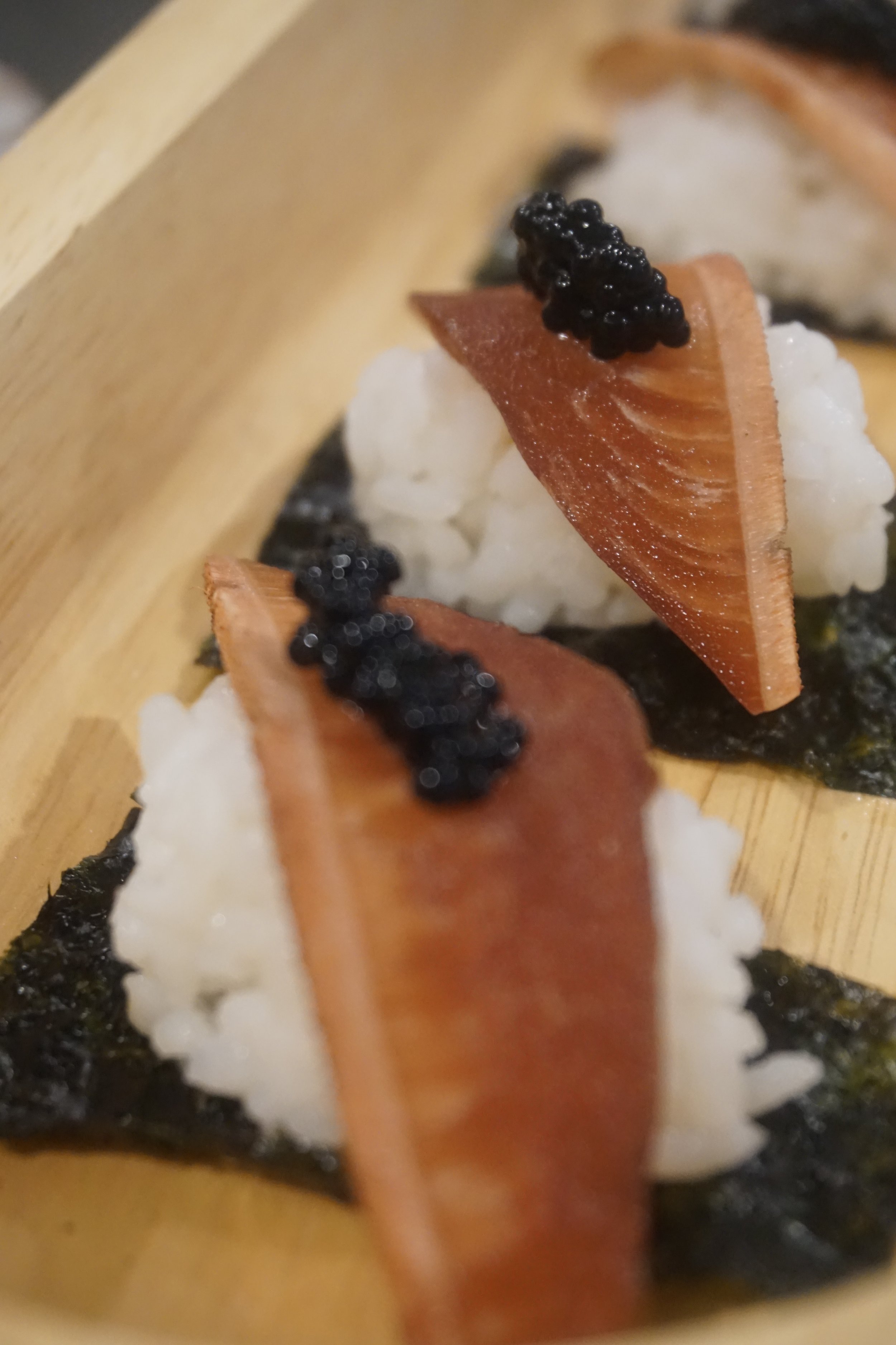 Close-up of sushi roll with rice, seaweed, a slice of fish, and caviar on top.