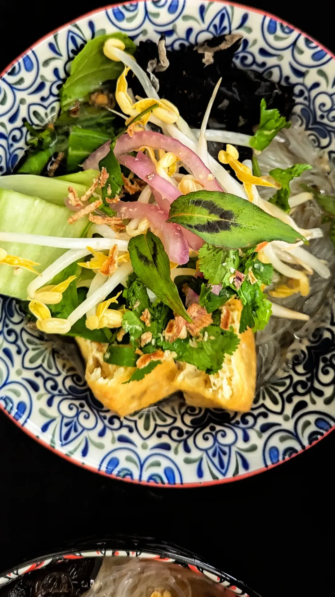 Colorful salad with vegetables, herbs, and fried tofu in a patterned bowl.