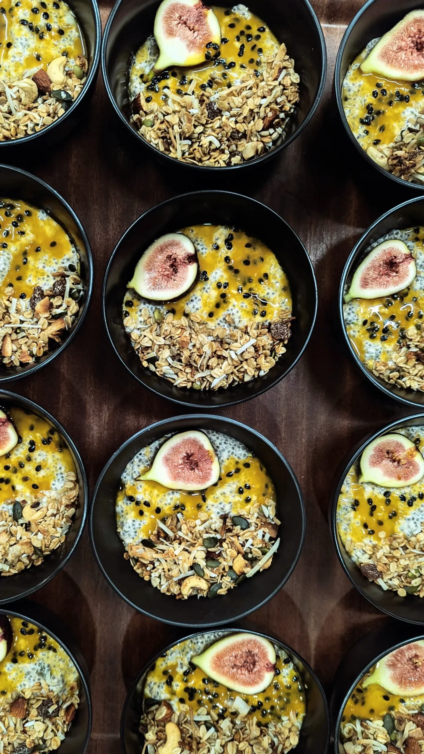 Bowls of yogurt topped with granola, sliced figs, and black berries, arranged on a wooden surface.