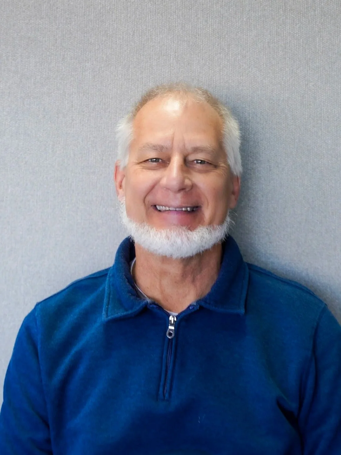 Older man smiling while sitting on outdoor steps, wearing a blue shirt.