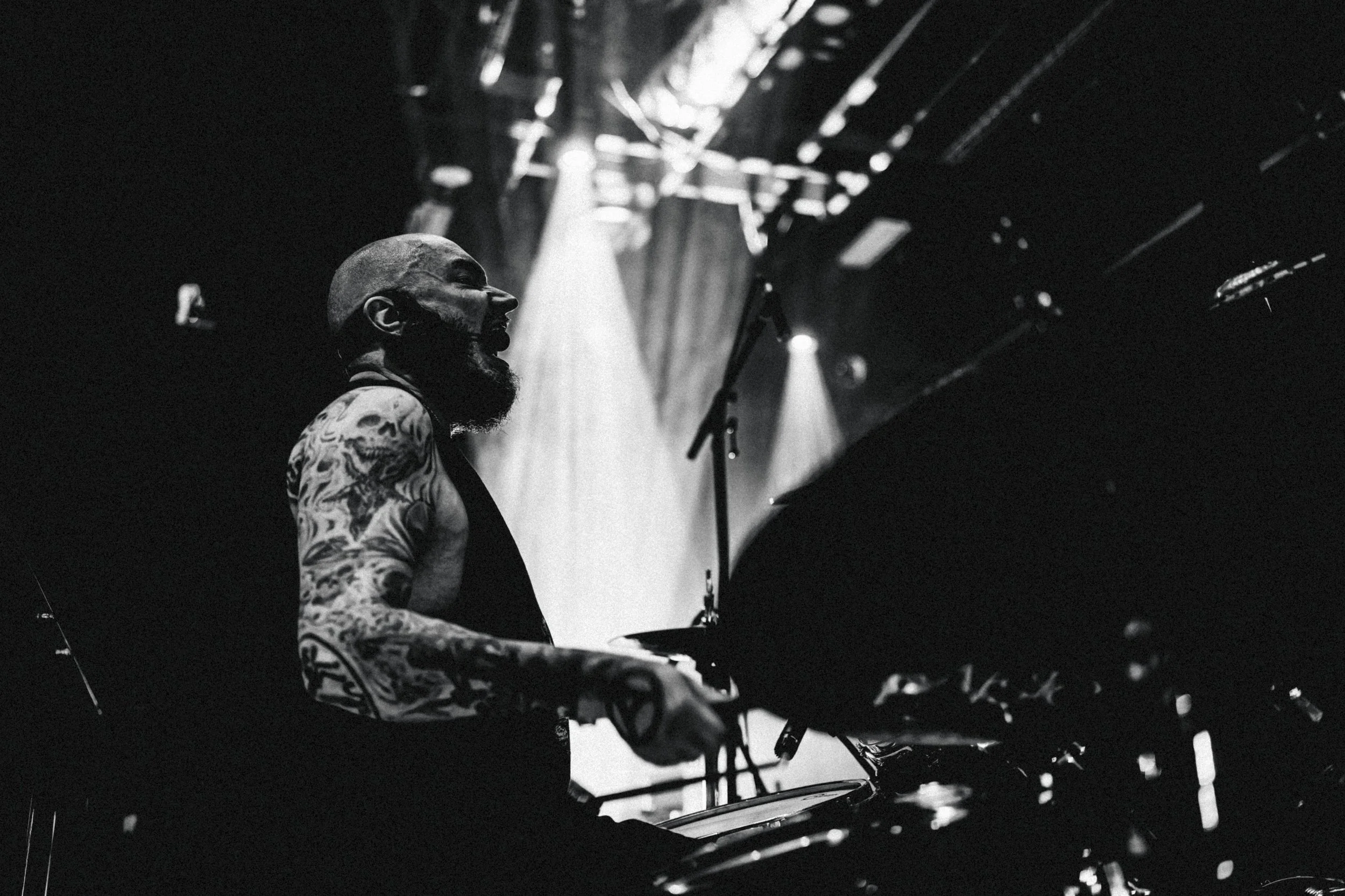 Musicien jouant de la batterie sur scène avec éclairage dramatique, en noir et blanc.