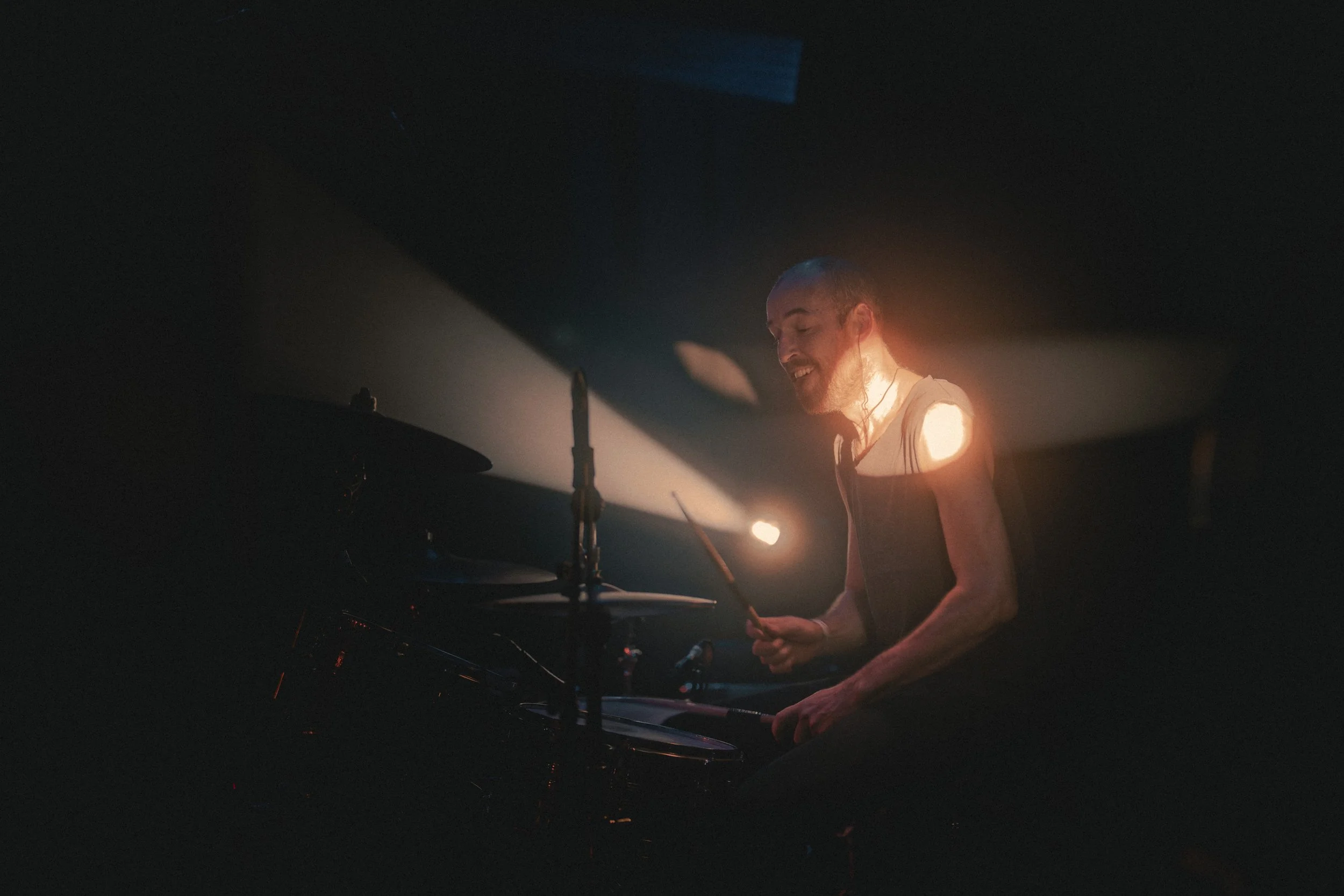 Un homme joue du piano sous un éclairage doux et chaud dans une ambiance sombre.