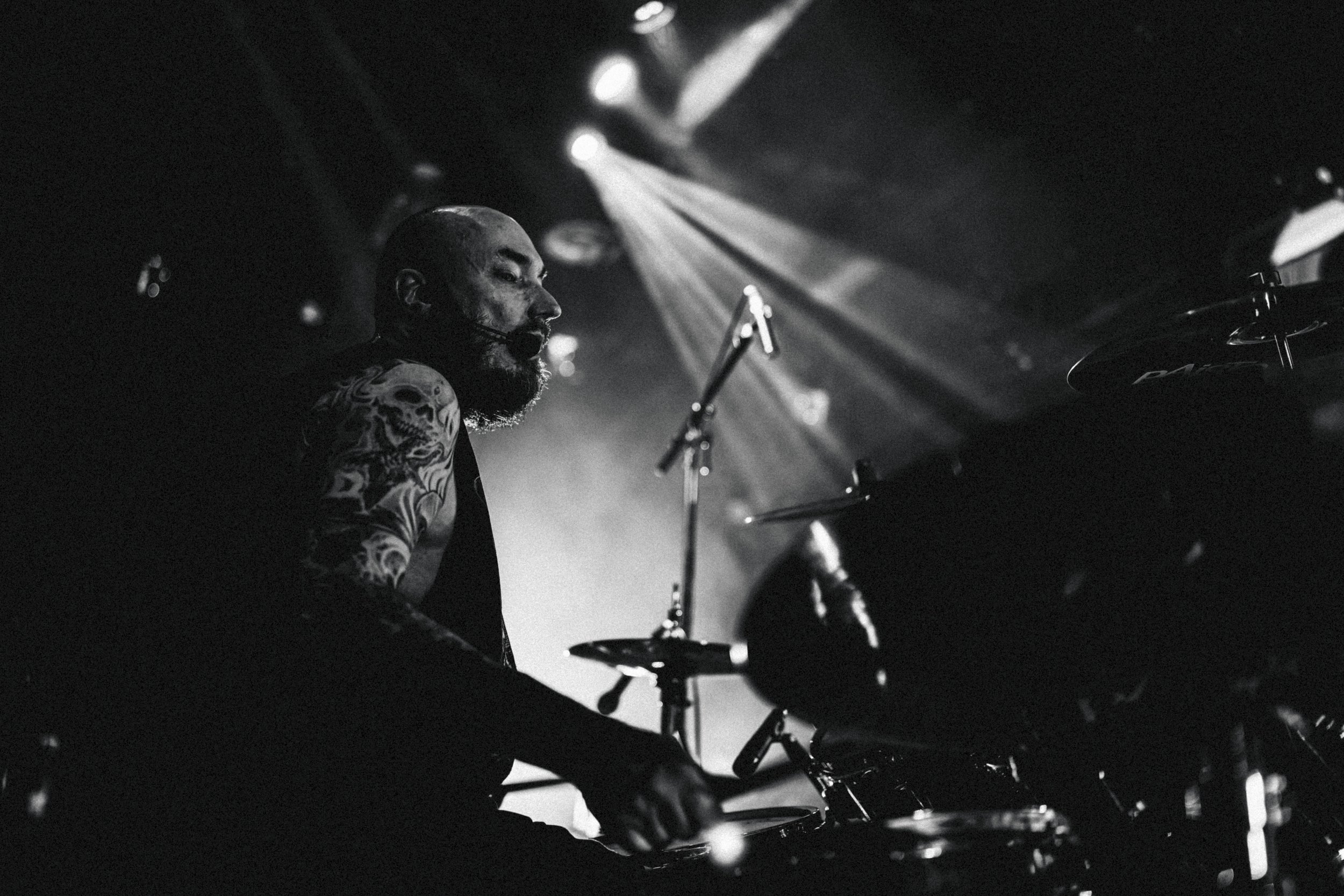 Musicien jouant de la batterie lors d'une performance sur scène, vue en noir et blanc.