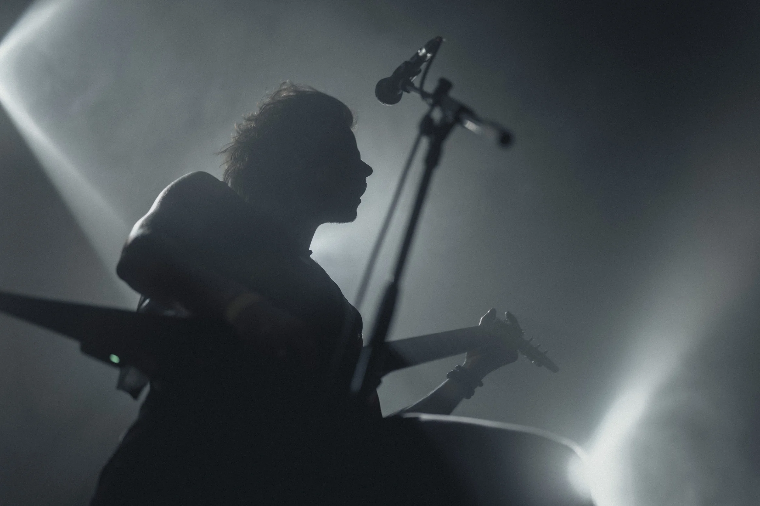 Silhouette d'une personne jouant de la guitare électrique, avec un microphone suspendu, dans un endroit sombre avec une lumière douce et ambiante.
