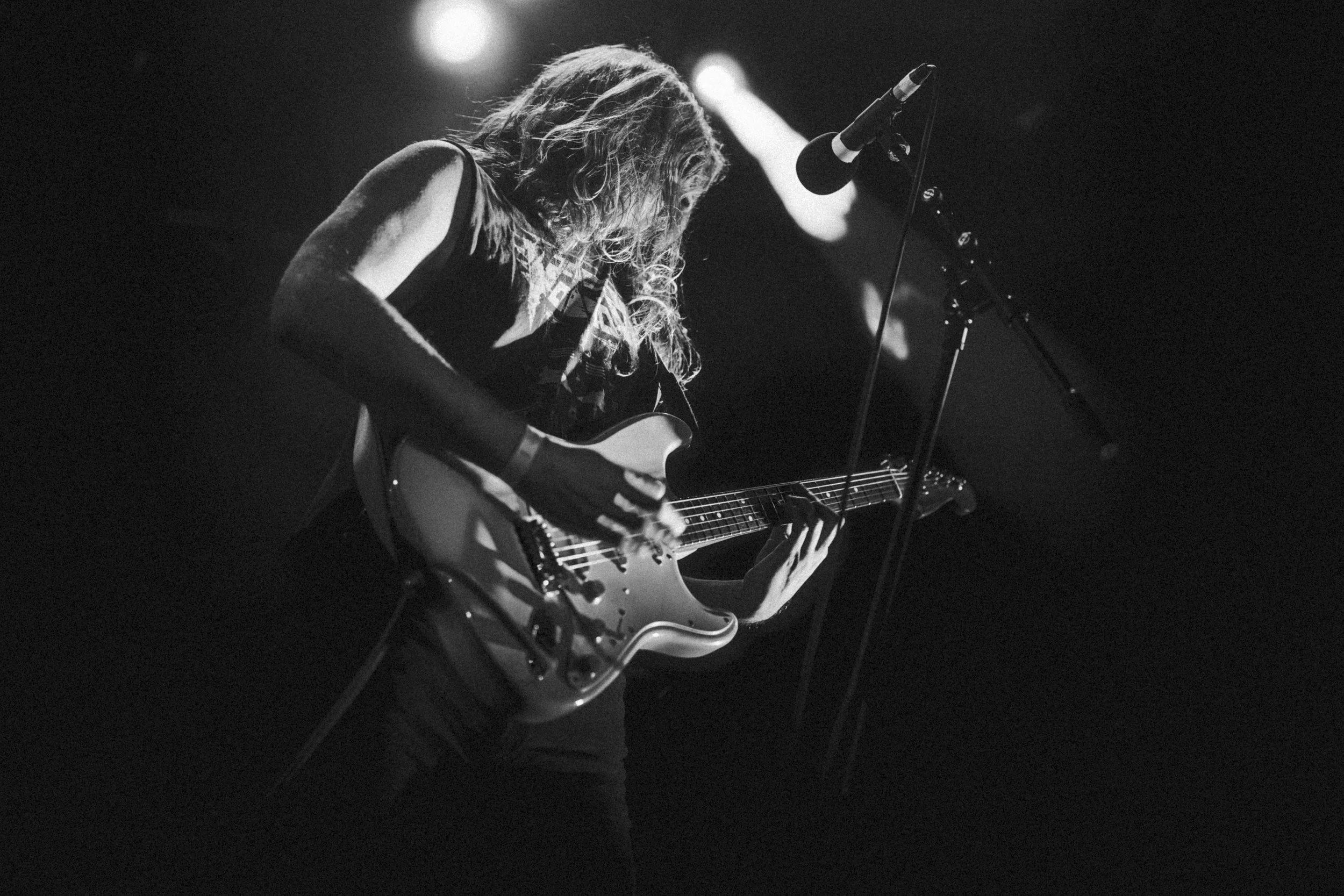 Une femme joue de la guitare électrique lors d'un concert, en noir et blanc, sous une lumière tamisée.