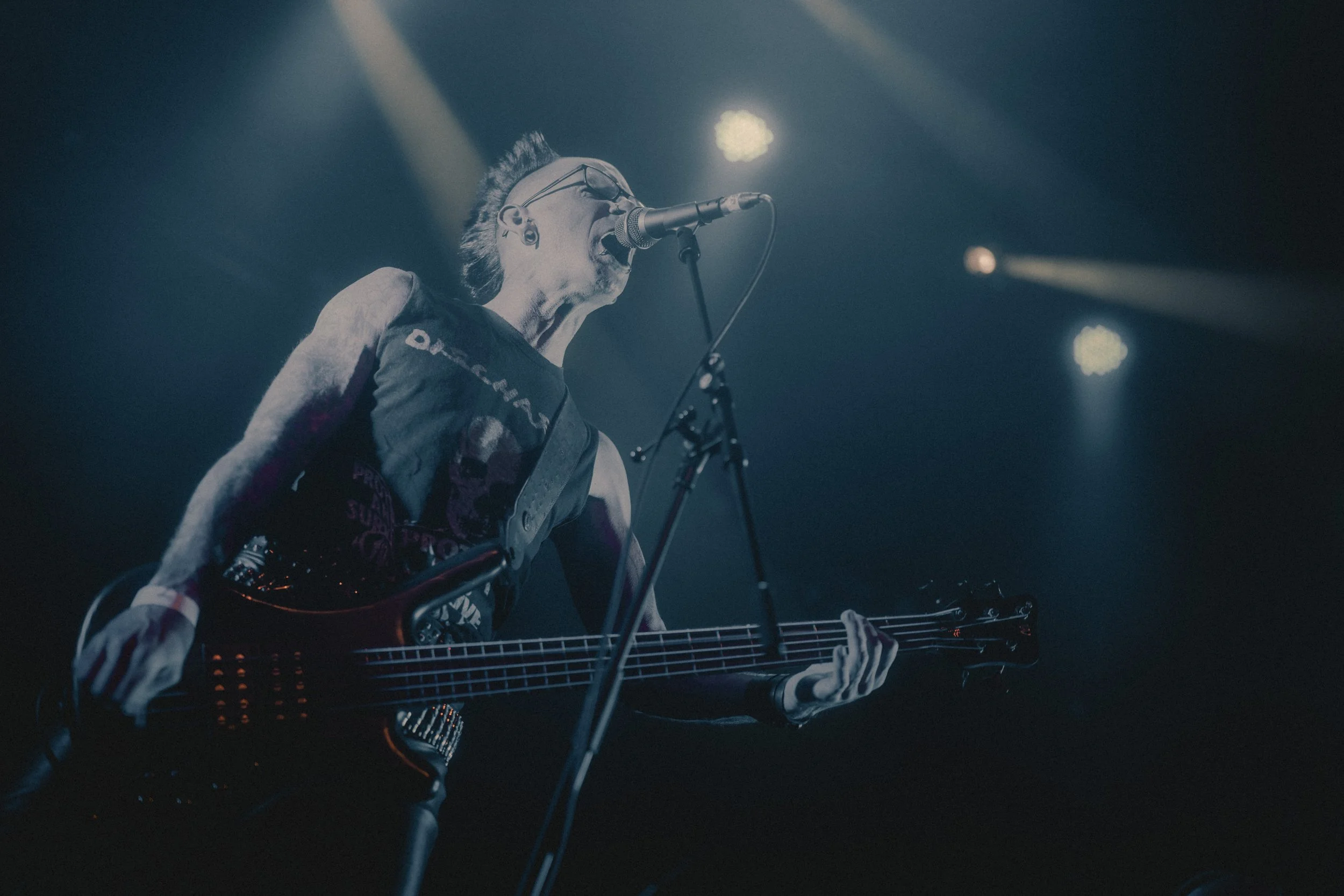 Musicien jouant de la basse électrique sur scène sous un éclairage tamisé, chantant dans un microphone.