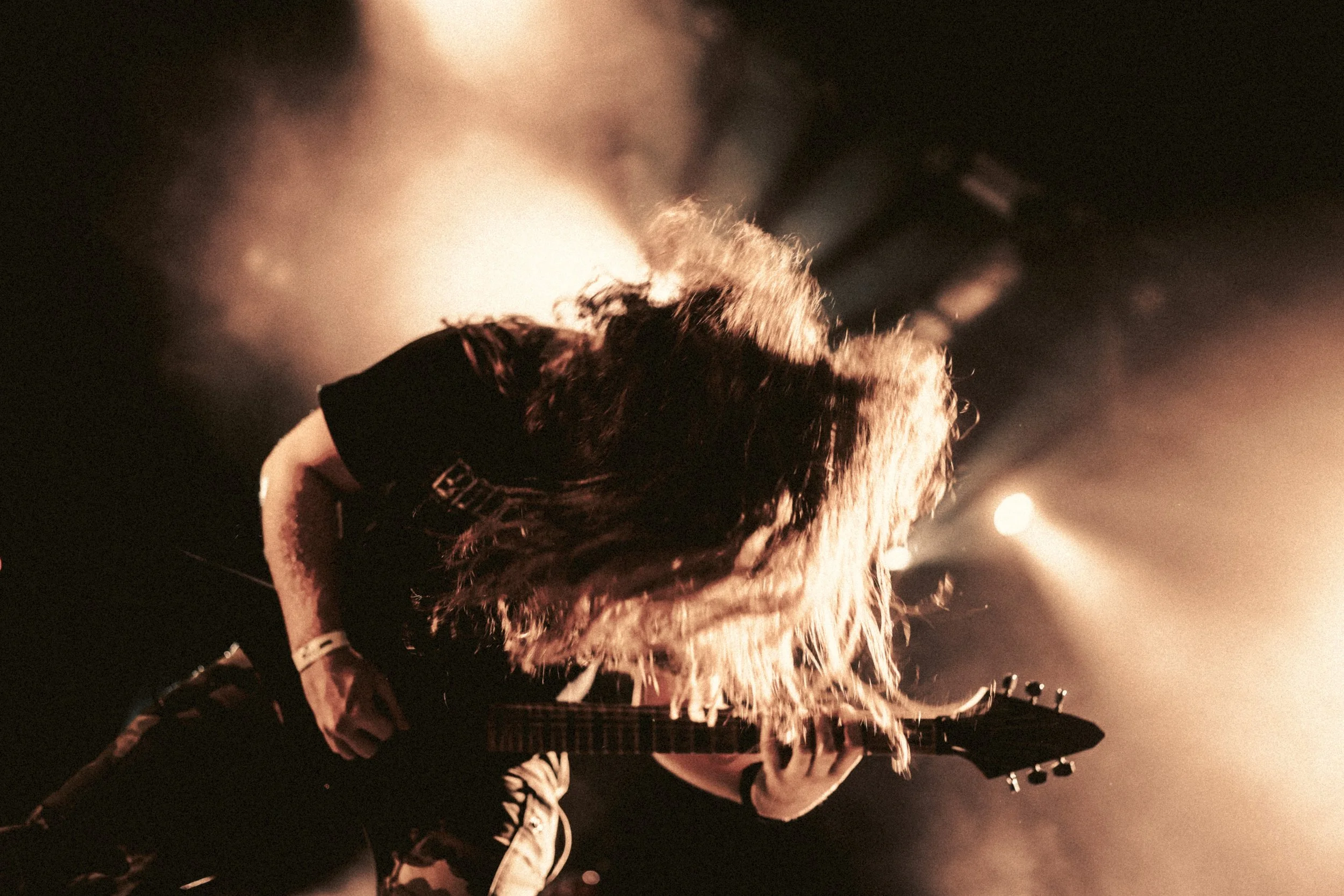 Musicien jouant de la guitare électrique en concert, éclairage chaud et ambiance sombre.