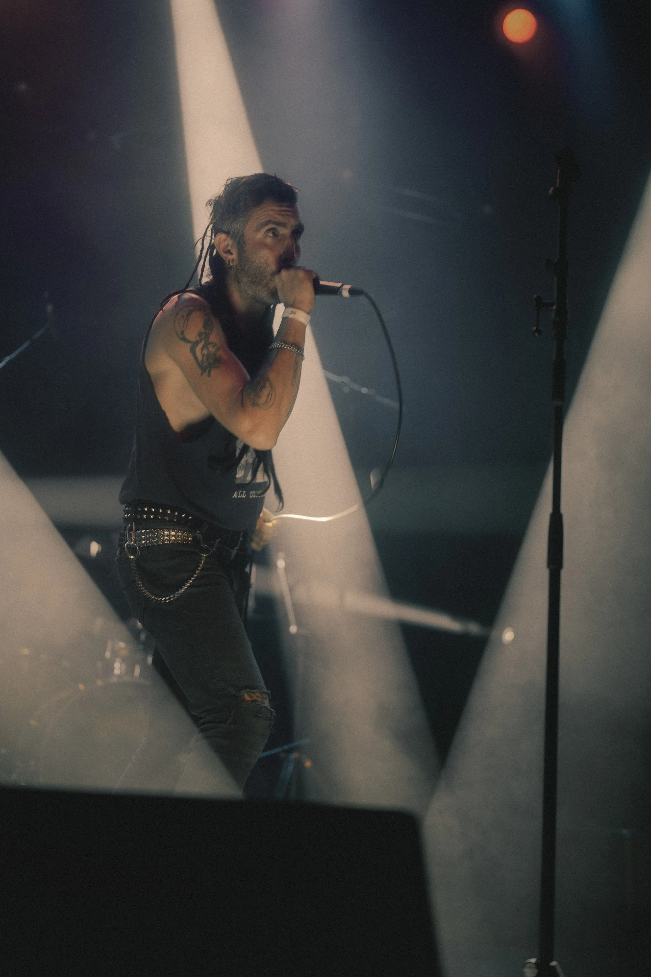 Un chanteur ou musicien en performance sur scène, tenant un microphone, avec des lumières de scène et un éclairage en arrière-plan.