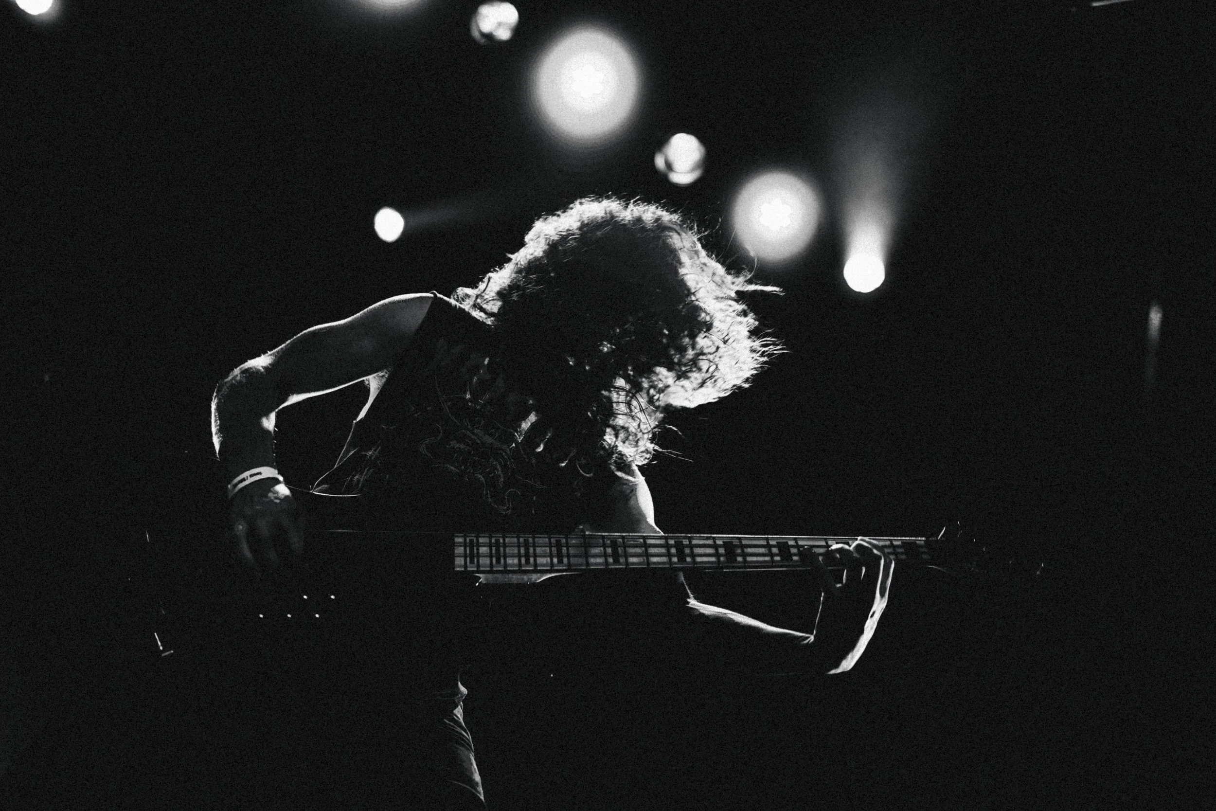 Un musicien joue de la guitare électrique sur scène, avec des lumières en arrière-plan créant une ambiance dramatique.
