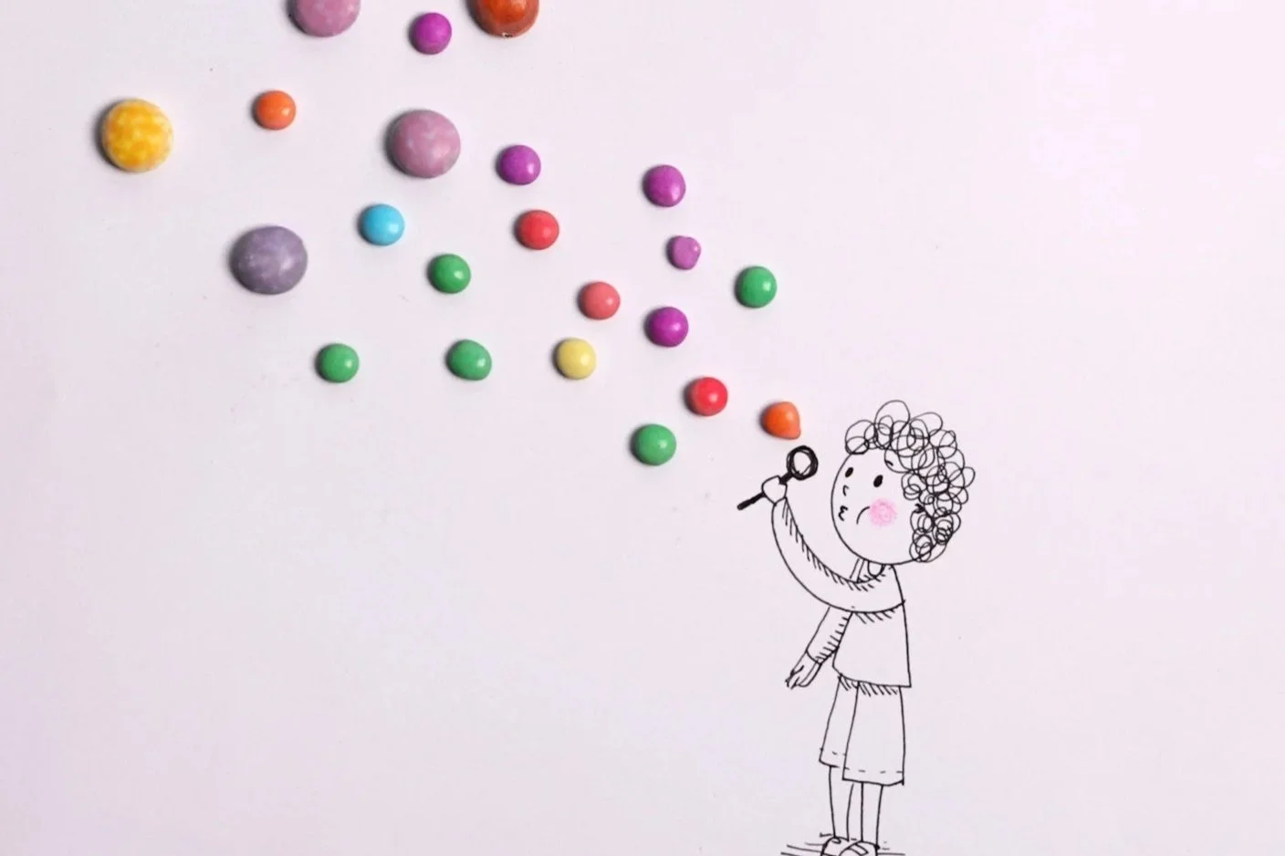 A hand-drawn girl with curly hair blowing bubbles made of colorful round candies or sweets, scattered in the air against a light background.