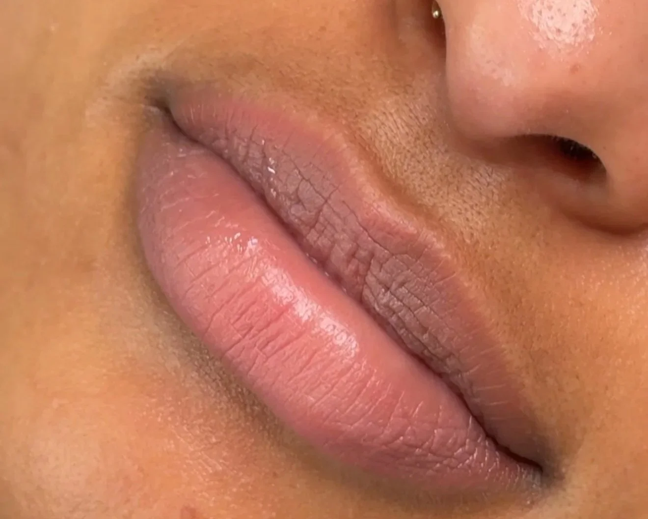 A close-up of a woman's face with makeup, showing glossy lips, defined eyebrows, and curled lashes.