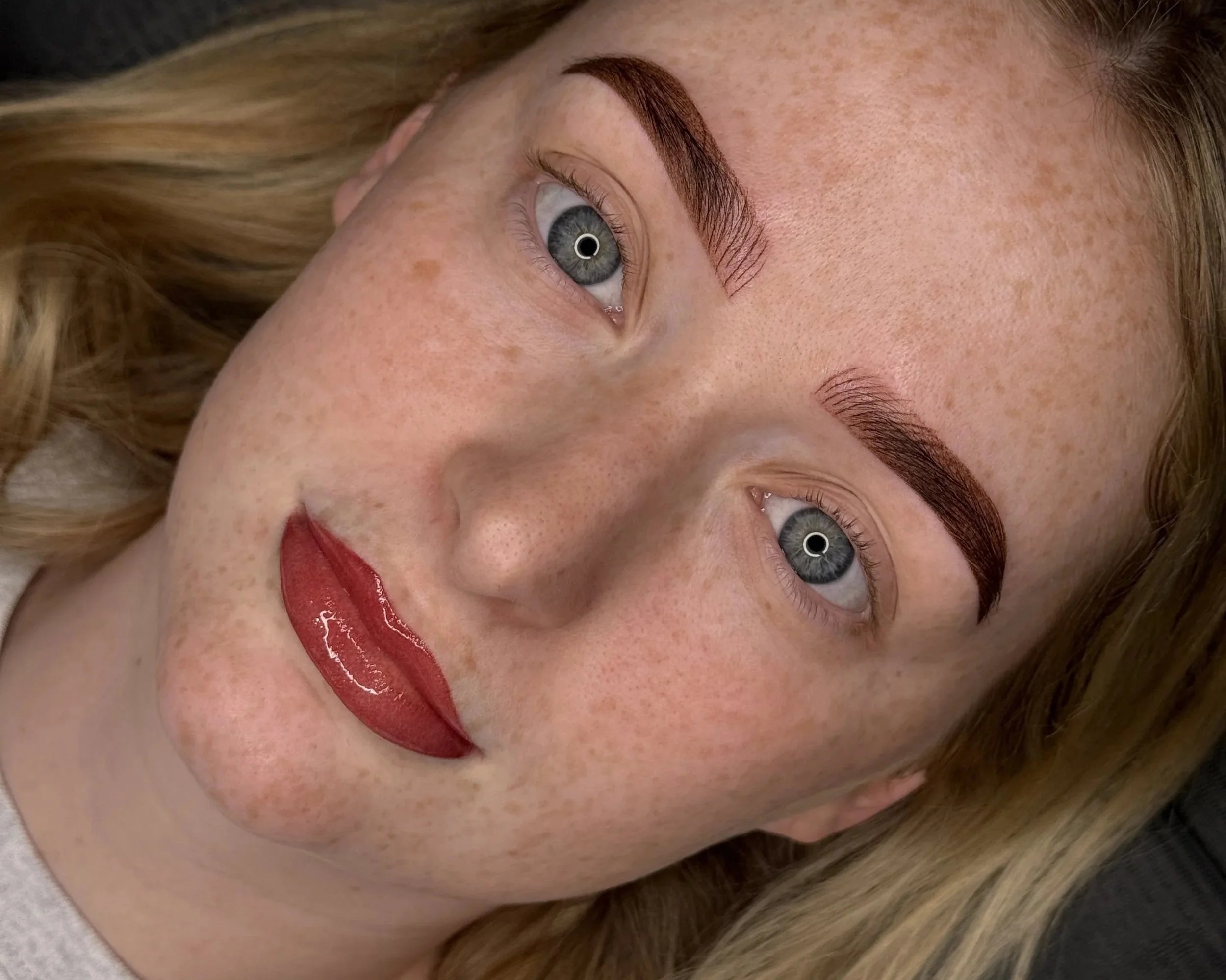 Close-up of a person with bold eyebrows, red glossy lips, and multiple facial piercings.