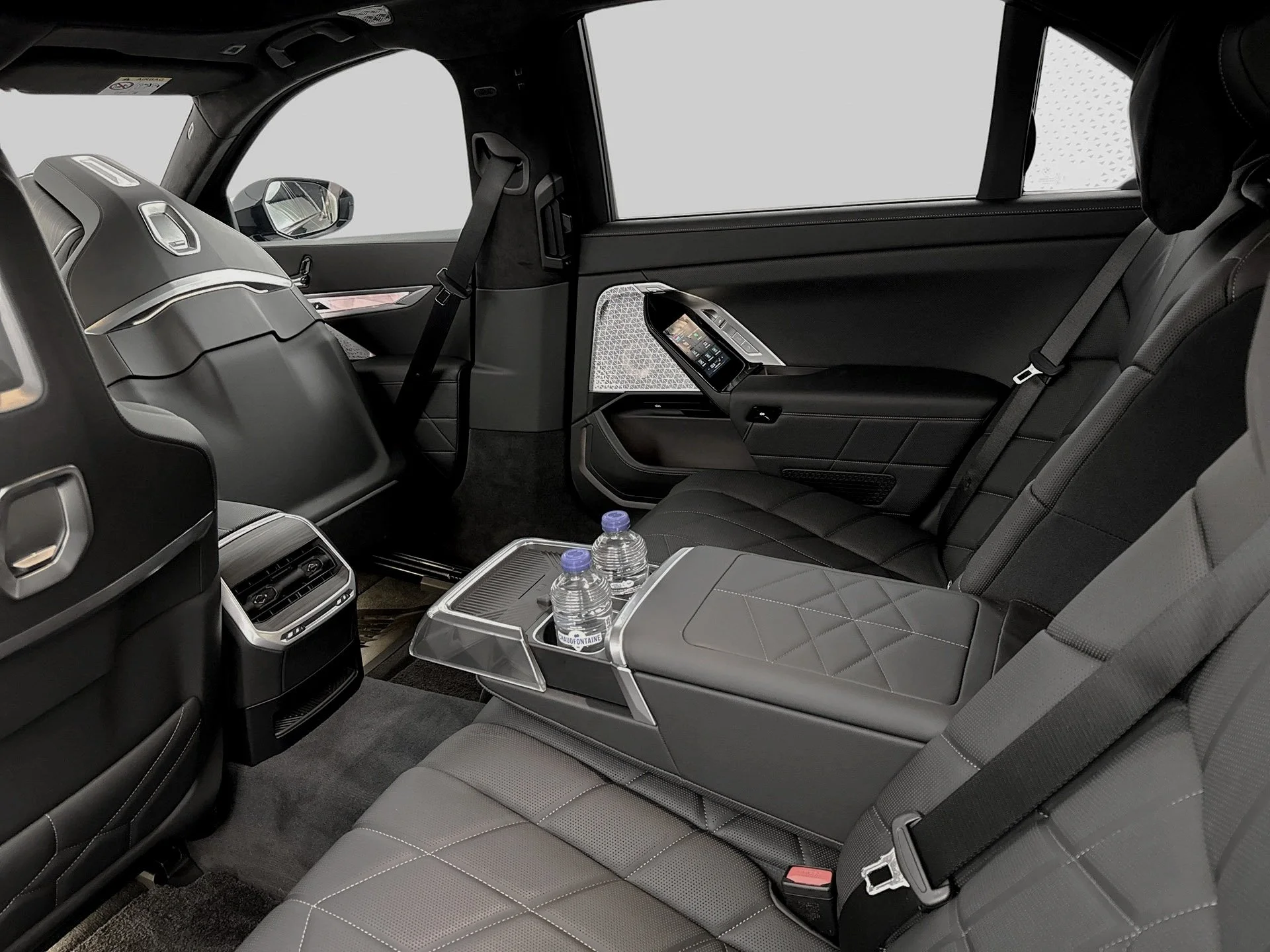 Interior of a luxury vehicle showing black leather seats with diamond stitching, a rear side window, and a center console with water bottles.